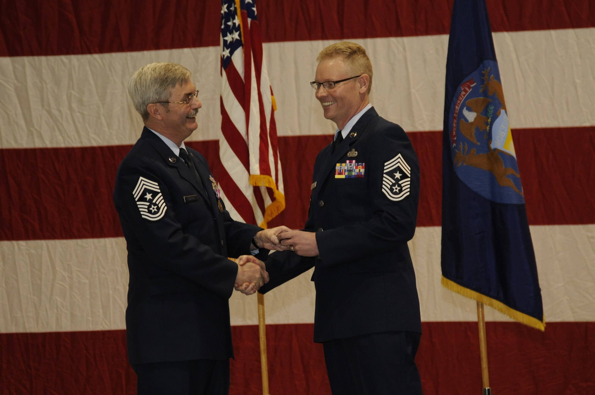Chief Master Sgt. Keith Edwards and Chief Master Sgt. Robert Dobson exchange a handshake during the ceremony in which Edwards relinquished his position as the command chief master sergeant of the 127th Wing of the Michigan Air National Guard, a role that is now held by Dobson. Edwards, who also retired in the ceremony, passed on his cell phone to Dobson during the ceremony, symbolizing the wing command chief’s responsibility to be a key advisor to the wing commander on all matters that pertain to the wing’s enlisted force. (U.S. Air Force photo by TSgt. David Kujawa)(RELEASED)