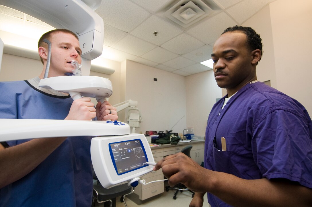 Navy Hospital Corpsman 1st Class Antonio Iglesia, Navy Branch Health Clinic expanded functions technician, programs a panoramic rotating machine to take a panoramic X-Ray of  Benjamin Maxfield, Navy information systems technician 2nd Class March 9. (U.S. Air Force photo/Bobby Jones)