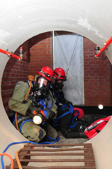 RAF MILDENHALL, England -- Firefighter Jerry Myles, left, and Crew Manager Dave Bootman, both 100th Civil Engineer Squadron Fire Department, check to see if they could take a "victim" back the way they came in. It was decided that the safest way to get the victim out was to use safety ropes lowered down by firefighters at the top of the facility, using a tripod and mechanical hauling system March 8, 2011, during a training exercise in the newly-built facility. The confined space trainer provides firefighters multiple ways of reaching a victim, allowing use of different equipment, depending on the scenario. Once inside, obstacles can be placed to simulate potential hazards, which make it more difficult for the rescuers to manouever a victim if a backboard, litter or basket has to be used. (U.S. Air Force photo/Karen Abeyasekere)