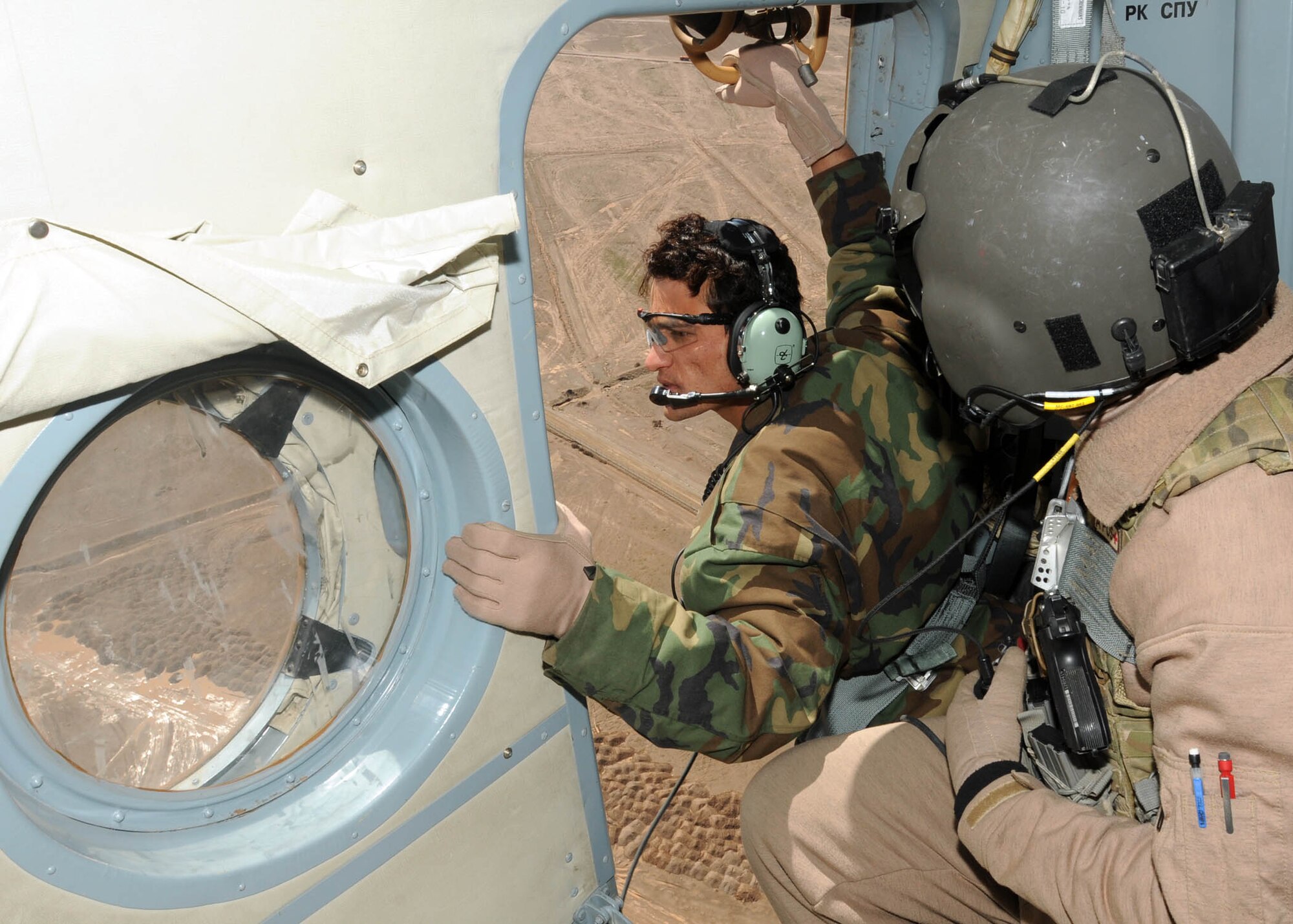 SHINDAND, Afghanistan - Afghan Air Force Staff Sgt. Mohammad Shafi, one of the Afghan flying crew chief students, make sure the Mi-17 is clear while Tech. Sgt. Travis Willingham, a flying crew chief air advisor, helps advise Staff Sgt. Shafi during his first flight mission at Shindand, Afghanistan. (U.S. Navy photo by Mass Communications Specialist 3rd Class Jared E. Walker). 
