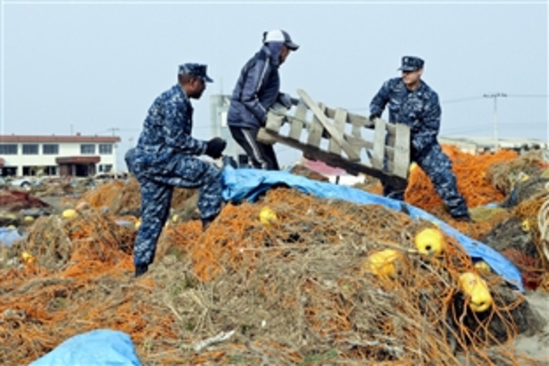U.S. Navy Petty Officer 2nd Class John and Petty Officer 1st Class Shakir Briggs help a Japanese man remove debris from the fishing port in Misawa, Japan, March 14, 2011. More than 90 sailors from Naval Air Facility Misawa volunteered in the relief effort, assisting Misawa City employees and members of the community. Dicola is an aerographer's mate and Briggs is an intelligence specialist assigned to the facility.