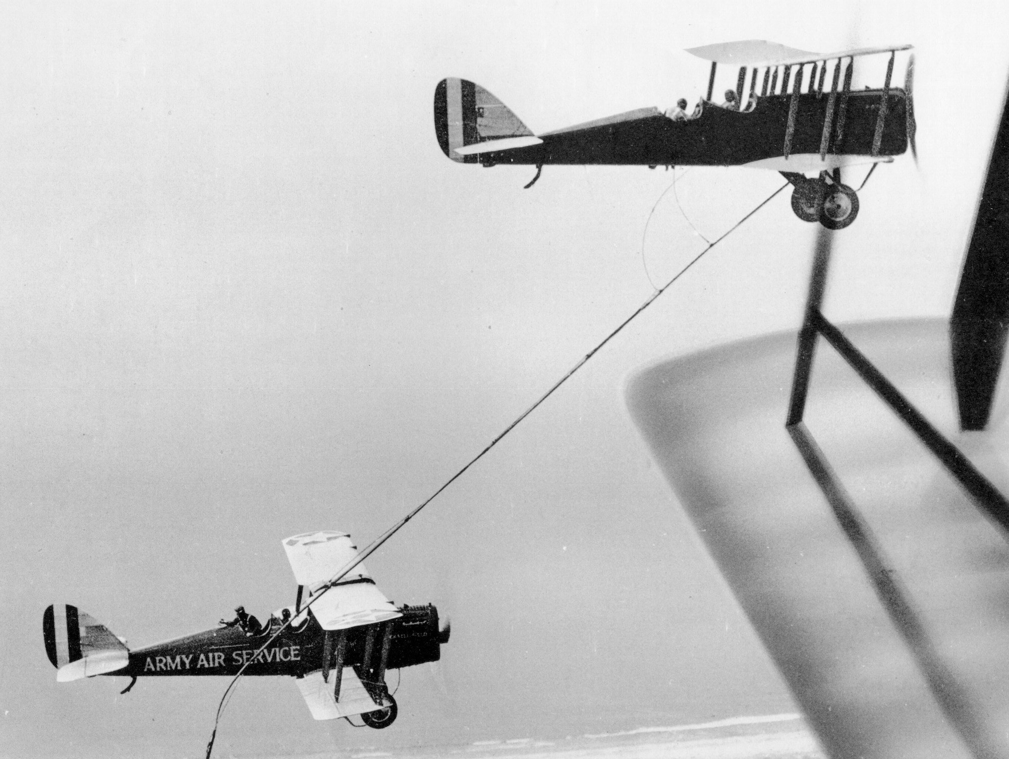 The de Havilland DH-4B tanker dangles a hose for the DH-4B receiver to grab over Rockwell Field.  In the tanker, 1st Lt. Frank W. Seifert holds the hose in the rear cockpit while the pilot, 1st Lt. Virgile Hine, is in the front.  Capt. Lowell H. Smith flew the receiver and 1st Lt. John P. Richter handled the hose.