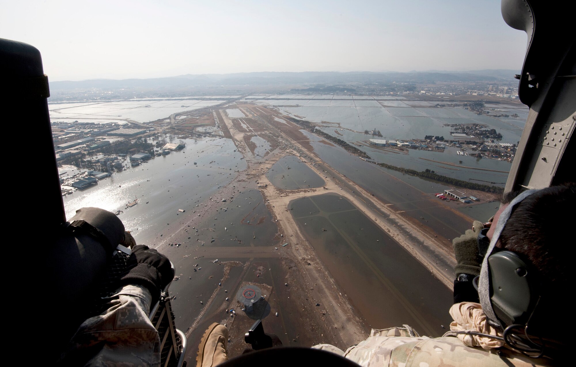 Airmen and Marines fly over the Sendai Airport, Japan, March 13, 2011, to survey the aftermath of the 8.9-magnitude earthquake and subsequent tsunami that struck the region. The small dots covering the runway are vehicles left there after the tsunami water receded. The service members are airlift and rescue leaders assisting with Japan's earthquake and tsunami recovery effort. (U.S. Air Force photo/Staff Sgt. Samuel Morse)