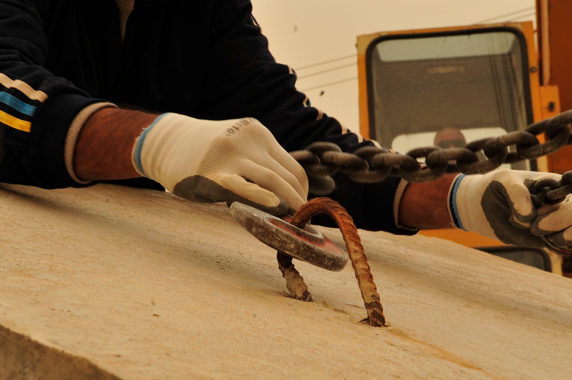 An Iraqi contractor holds steel chains from a 10 to 20 ton crane in place, as a crane operator awaits a signal to lift a 6-ton concrete T-wall barrier onto an awaiting flatbed truck, March 3, 2011, at Victory Base Complex in Baghdad. These crews are supporting a partnered effort to turn-over 1,200 U.S. forces T-walls to the Iraqi Army. The work they're doing took place during the orange haze of a sand storm in the Iraqi desert. Each T-wall is 12-feet tall. (U.S. Air Force photo by Senior Master Sgt. Larry Schneck)