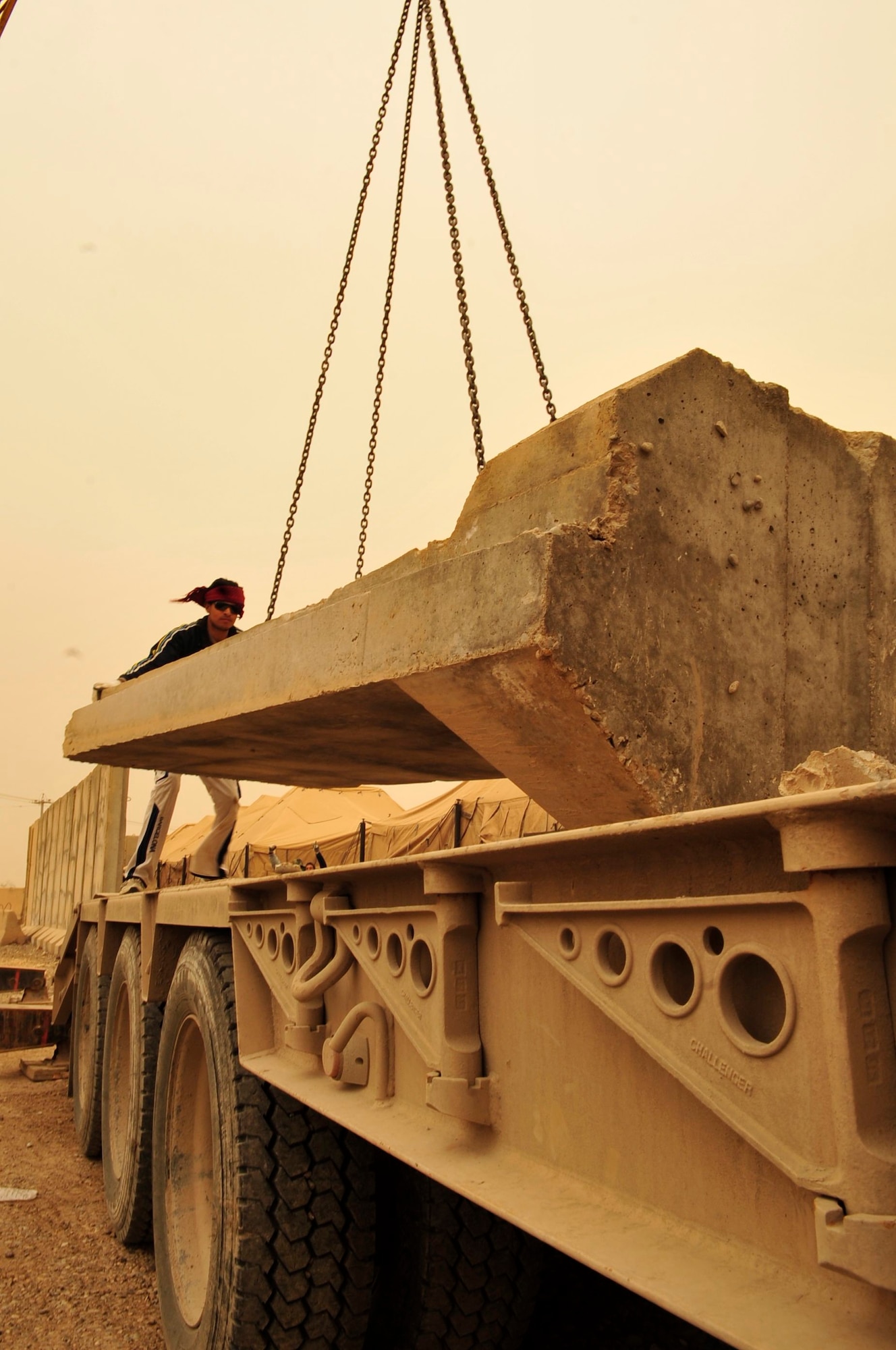 In the middle of an orange haze during a sand storm in the Iraqi desert, an Iraqi contractor rigs a T-wall concrete barrier onto a flatbed truck, March 3, 2011, at Victory Base Complex in Baghdad. This local-national contractor is supporting a partnered effort to turn-over 1,200 U.S. forces T-walls to the Iraqi Army. A T-wall weighs 6 tons and is 12-feet tall. It requires the force of a ten to twenty-ton crane to relocate each one. (U.S. Air Force photo by Senior Master Sgt. Larry Schneck)