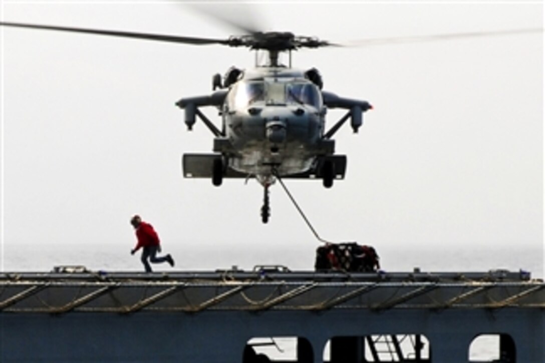 An MH-60S Seahawk helicopter transports humanitarian assistance supplies from the Military Sealift Command dry cargo and ammunition ship USNS Matthew Perry (T-AKE 9) to the amphibious assault ship USS Essex (LHD 2) in the Philippine Sea on March 15, 2011.  The Essex is underway to Japan to provide humanitarian assistance as directed in support of Operation Tomodachi.  