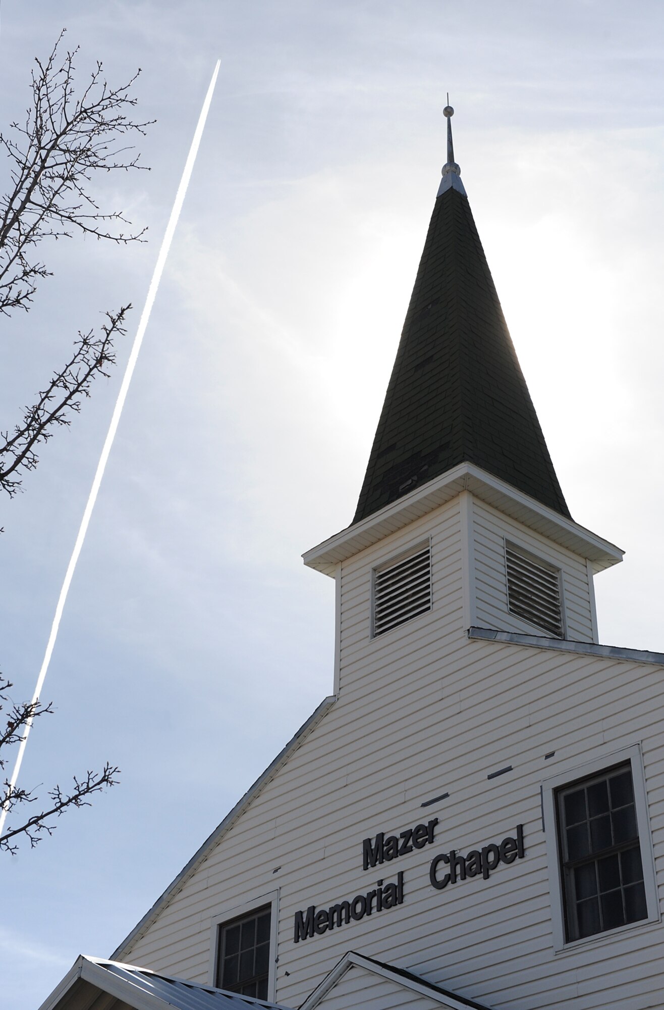 A Boeing 737 jet airliner leaves a contrail at the newly renames Mazer Memorial Chapel, formerly the Hill Historic Chapel, March 11. The ceremony and renaming was in tribute to Col. Nathan Mazer, who was instrumental in saving the structure and having it restored to its current status and use. He died in 2006. (U.S. Air Force photo by Alex Lloyd)