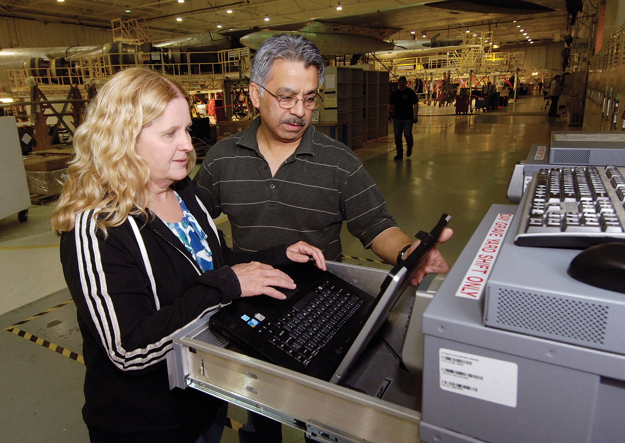 Vincent Equigua and Belinda Stephens, both with the 72nd Communications Directorate, demonstrate the new E-tool cabinets that hold Toughbook laptop computers for checkout by mechanics.  Within feet of a B-52 in a depot hangar, the racks offer rugged computers to replace paper technical orders and repair information that can travel with the mechanics as they work anywhere on the aircraft. Information updates are downloaded at night when the computers are stored in the rack system. (Air Force photo by Margo Wright)