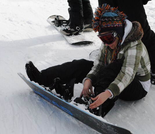 Airman 1st Class Courtney Taylor, a 341st Comptroller Squadron customer service technician, takes a break to fix a strap on her snowboard.  Airman Taylor along with several others enjoyed an abundance of snow and sunshine on the final Wing Ski Day this winter.  (U.S. Air Force photo/Airman Cortney Hansen)