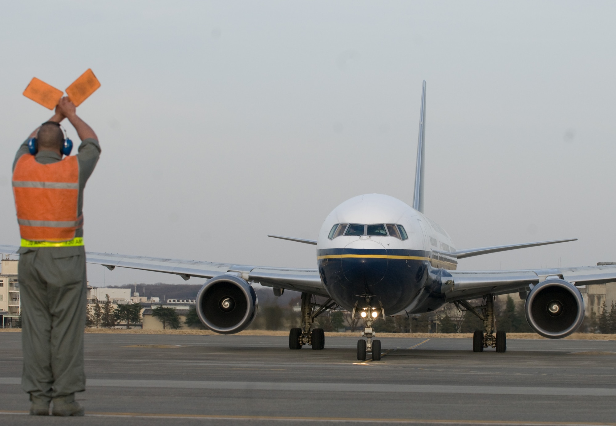 YOKOTA AIR BASE, Japan -- Senior Airman Daniel Ramos, 730th Air Mobility Squadron crewchief, marshals a Boeing-767 aircraft out for takeoff here March 19. The aircraft, along with 233 passengers, is part of the first voluntary authorized departure flight from Yokota. (U.S. Air Force photo/Staff Sgt. Robin Stanchak) 