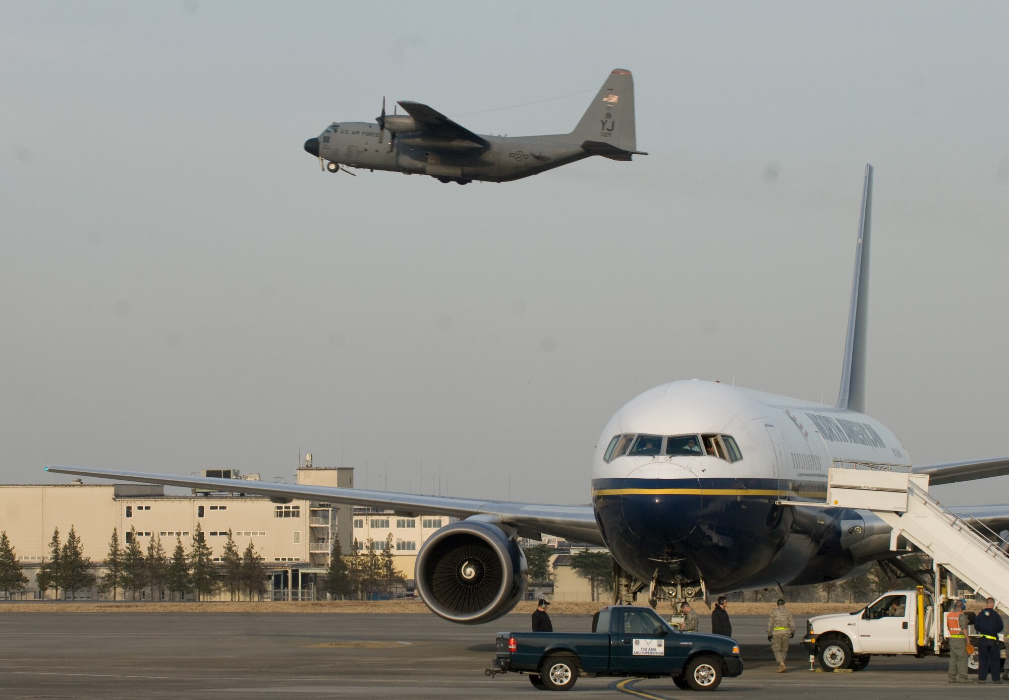 YOKOTA AIR BASE, Japan -- A Boeing-767 aircraft sits on the runway here as a C-130 Hercules takes off March 19. The B-767 aircraft was the first to transport 233 passengers as part of the voluntary authorized departure from Yokota. (U.S. Air Force photo/Staff Sgt. Robin Stanchak) 