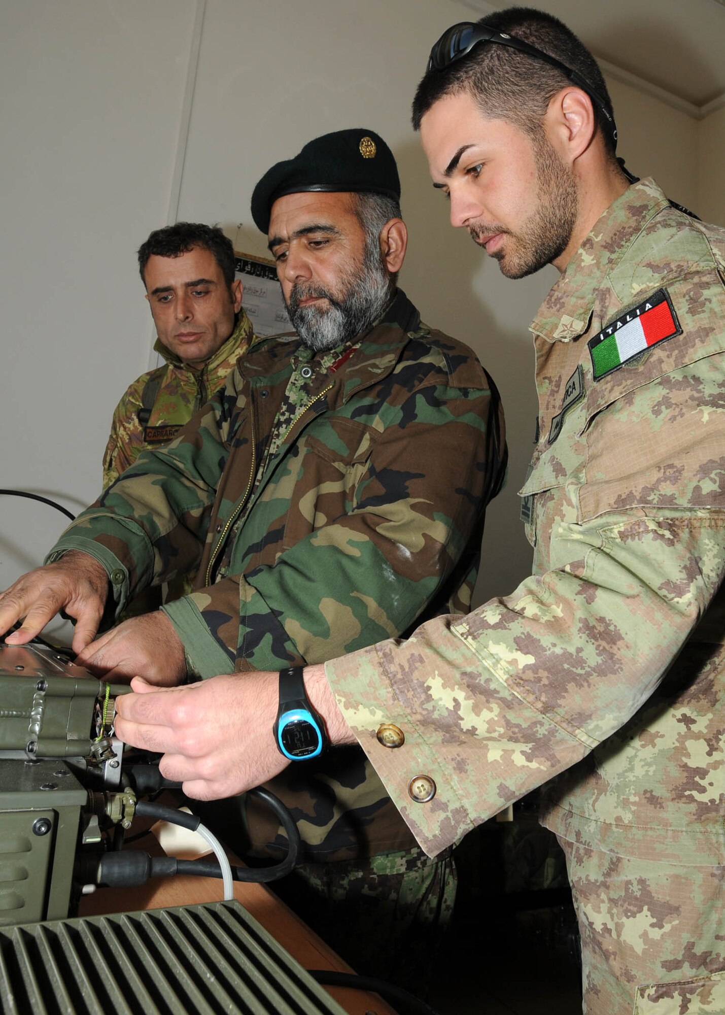 SHINDAND, Afghanistan - Italian Air Force service member, with NATO Training Mission - Afghanistan / 838th Air Expeditionary Advisory Group, assists a member of the Afghan Air Force while he works on radio equipment in Shindand, Afghanistan. (U.S. Navy photo by Mass Communications Specialist 3rd Class Jared E. Walker).