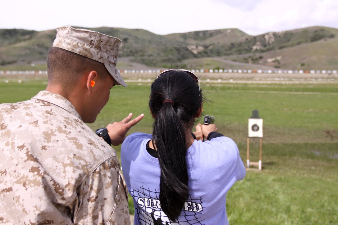 Carmen Rodriguez, a Headquarters and Support Battalion spouse, is coached on pistol marksmanship techniques by Cpl. Dane Davis, Combat Logistics Regiment 1, 1st Marine Logistics Group, at the annual John/Jane Wayne Day held at Camp Pendleton, March 19. The family members were welcomed to John/Jane Wayne Day and given the opportunity to see what their Marines do on a daily basis. Events included a Combat Fitness Test, rifle and pistol shooting, a Marine Corps Martial Arts Program lesson, an Explosive Ordnance Disposal display, and a military working dog demonstration.