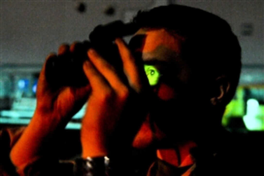 U.S. Navy Petty Officer 2nd Class Jordan Lochmann uses night vision binoculars to scan the horizon for Tomahawk missile trails from the flight deck of amphibious assault ship USS Kearsarge during strike missions supporting Operation Odyssey Dawn in the Mediterranean Sea, March 19, 2011.