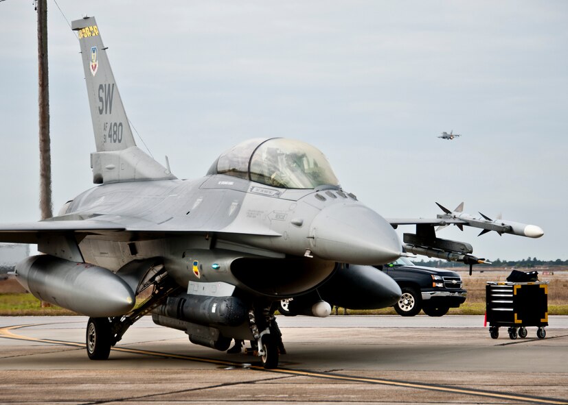 A 20th Fighter Wing F-16 Fighting Falcon waits to taxi as another F-16 climbs into the gray skies at Eglin Air Force Base, Fla. March 14.  More than 10 F-16s from the 20th Fighter Wing were on hand to participate in the air-to-ground weapons system evaluation program known as Combat Hammer at Eglin.  The week-long evaluation is conducted by the 86th Fighter Weapons Squadron, located here.  The squadron hosts 20 to 25 evaluations at Hill and Eglin each year, assessing weapon system performance, reliability, capabilities, and limitations in realistic combat scenarios against representative real-world targets.  (U.S. Air Force photo/Samuel King Jr.)
