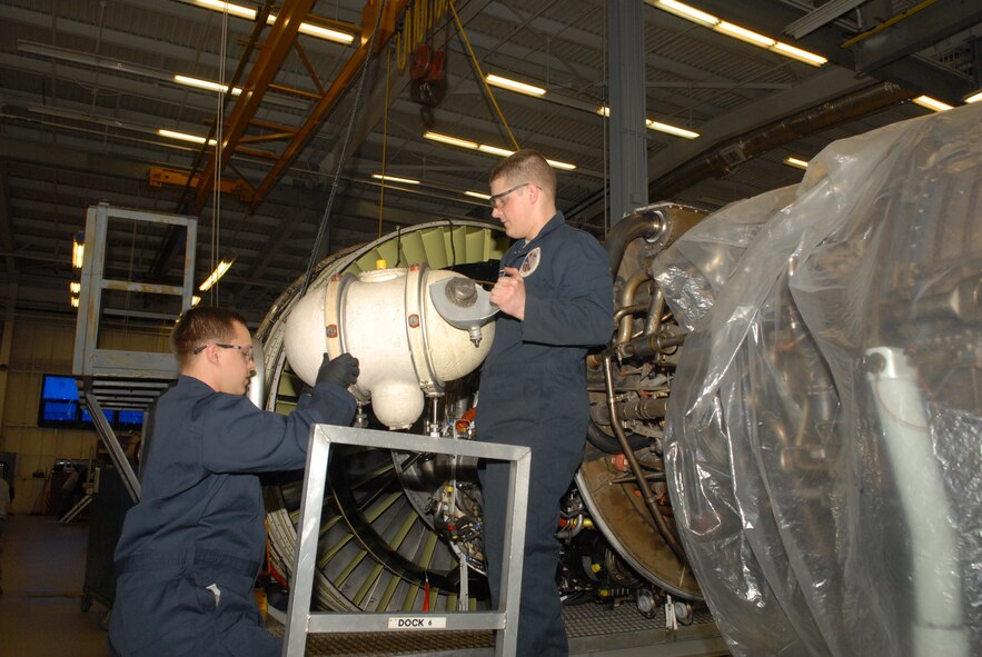 Senior Airman Anthony Ash (left) and Senior Airman Corey Brydon, 436th Maintenance Squadron aerospace propulsion technicians, replace a TF-39 engine’s oil tank at Dover Air Force Base, Del. Jet Engine Intermediate Maintenance shop March 16, 2011. In the background, the TF-39 is lifted slightly off the ground and sat on a docking station within the shop. (U.S. Air Force photo by Airman 1st Class Jacob Morgan)