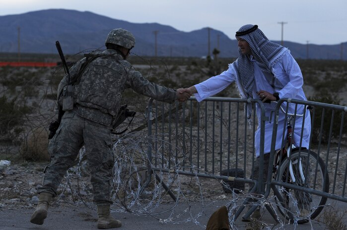 NEVADA TEST AND TRAINING RANGE -- Senior Airman Bryan Webb, 820th Base Defense Group, Airman dressed as Iraqi villager, shake hands over fence separating the base from the village during a field training exercise at exercise Desert Eagle March 14. Desert Eagle is integrated training between No.1 Squadron, RAF Regiment and the 820th Base Defense Group Moody Air Force Base Ga., to improve both nations ability to work together during present and future contingencies. (U.S. Air Force photo by Airman 1st Class Daniel Hughes)