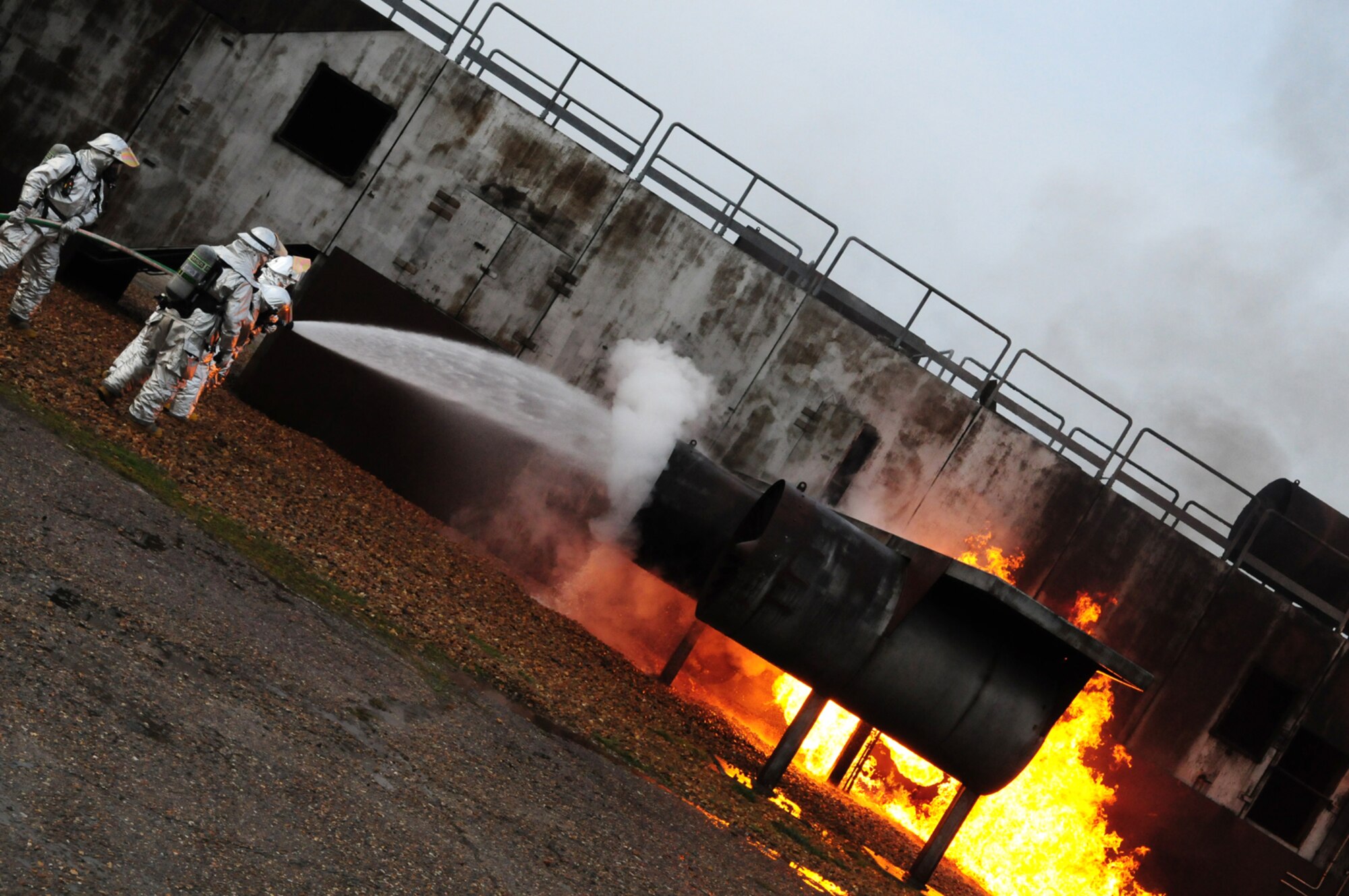 RAF MILDENHALL, England -- Firefighters from the 100th Civil Engineer Squadron assist Nigel McCurdy, right, Forest Heath District Council strategic director and 100th CES honorary commander, use a pressurized hose to put out a fire on a mock aircraft engine at the live fire trainer here March 17, 2011. Mr. McCurdy and Col. David Doe, 100th Mission Support Group commander, spent time training with the firefighters to get an insight into what goes into their training and the job they do. The two men donned protective equipment weighing about 70 pounds and helped put out a fire, as well as going into the smoke house and performing a simulated rescue, when they had to bring out a mannequin with the aid of one of the firefighters. (U.S. Air Force photo/Karen Abeyasekere)
