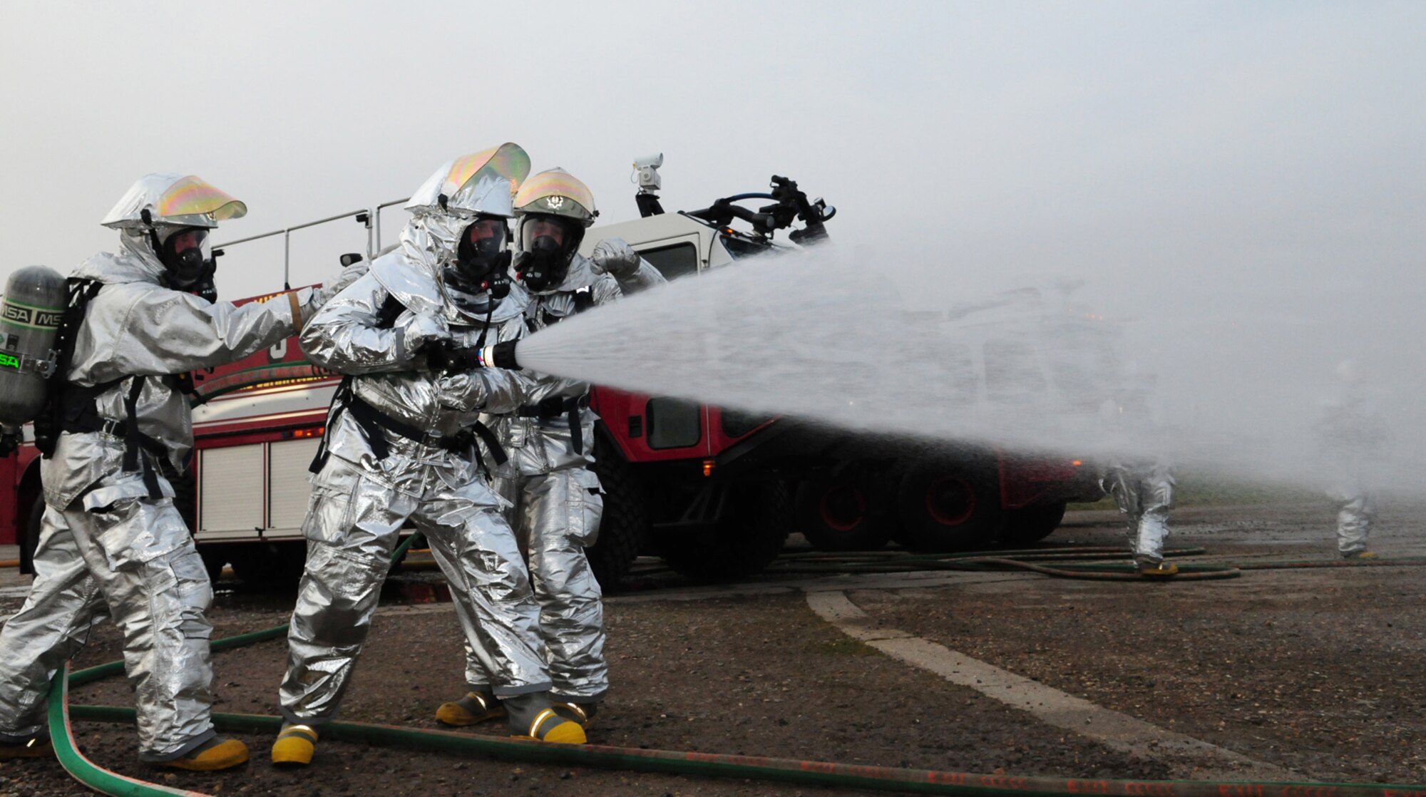 RAF MILDENHALL, England -- Nigel McCurdy, center, Forest Heath District Council strategic director and 100th Civil Engineer Squadron honorary commander, uses a pressurized hose to put out flames on a mock aircraft at the live fire trainer here March 17, 2011, assisted by crew managers Barry Clark and Simon Evans, both Defence Fire Service firefighters with the 100th CES Fire Department. Mr. McCurdy, along with Col. David Doe, 100th Mission Support Group commander, had the opportunity to train with the firefighters and wear about 75 pounds of protective equipment, which included bunkers, boots and breathing apparatus. (U.S. Air Force photo/Karen Abeyasekere)