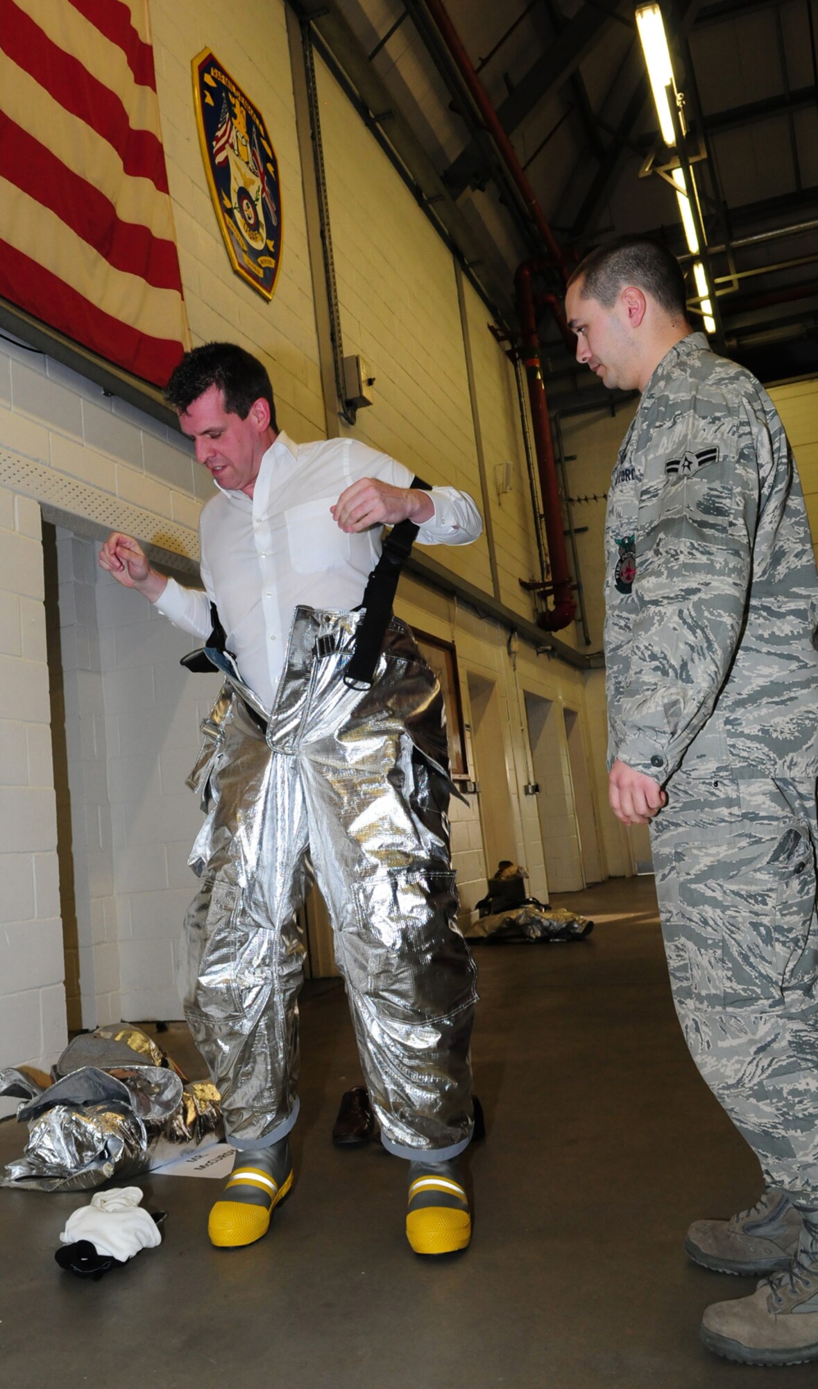 RAF MILDENHALL, England -- Nigel McCurdy, Forest Heath District Council strategic director and 100th Civil Engineer Squadron honorary commander, puts on a firefighter's silver bunkers, overseen by Airman 1st Class Ryan Carrillo, 100th CES Fire Department, in preparation for live fire training here March 17, 2011. Mr. McCurdy, and Col. David Doe, 100th Mission Support Group commander, had the opportunity to don protective gear and help put out a fire at the mock aircraft, assisted by base firefighters. (U.S. Air Force photo/Karen Abeyasekere)