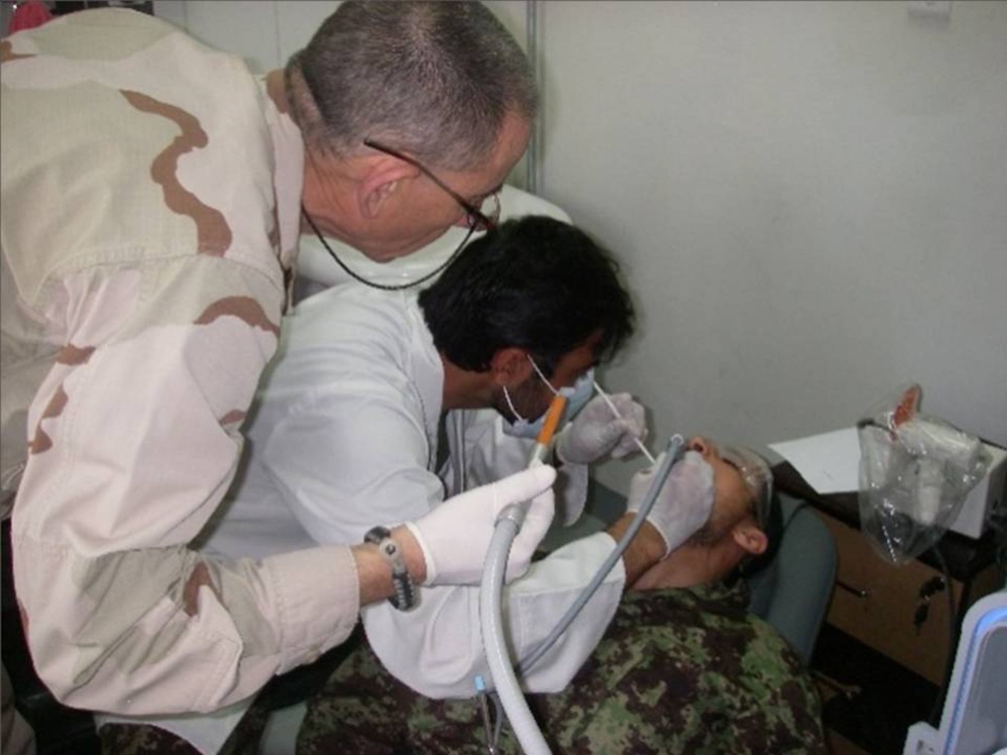 Lt.Cmdr. Sholi Rotblatt, a dentist in the U.S Navy Reserves deployed to Afghanistan, looks on as Dr. Basir of the Kandahar Air Wing extracts an infected tooth from the mouth of an Afghan Air Force Airmen at the KAW Medicine Clinic March 17. (U.S. Air Force courtesy photo)