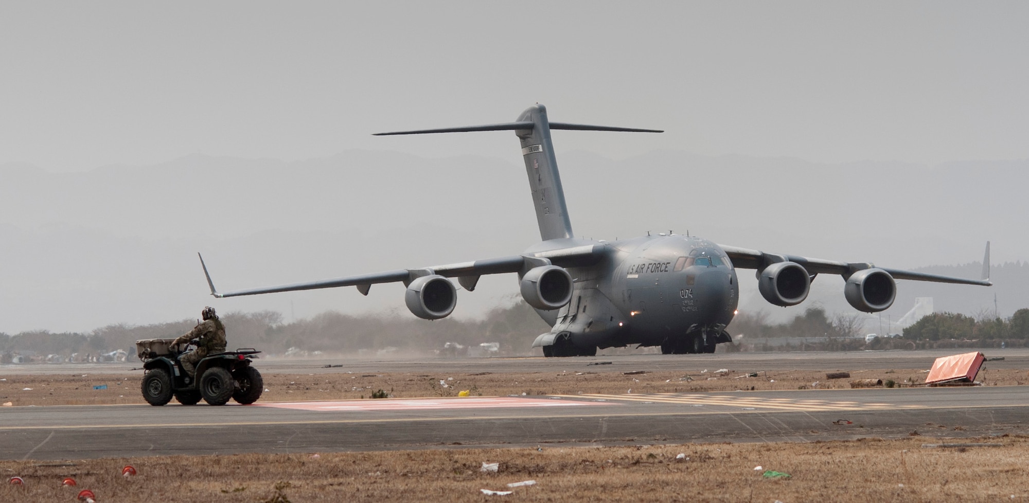 A combat controller from the 320th Special Tactics Squadron from Kadena Air Base, Japan, waits for a C-17 Globemaster III to taxi back after landing at Sendai Airport March 20. The combat controller used his all-terrain vehichle as a "follow me" car to guide the C-17 to its cargo offload point. Sendai Airport has become a main hub for bringing humanitarian aid to those affected by the earthquake and tsunami from March 11.  (U.S. Air Force photo/Staff Sgt Samuel Morse)