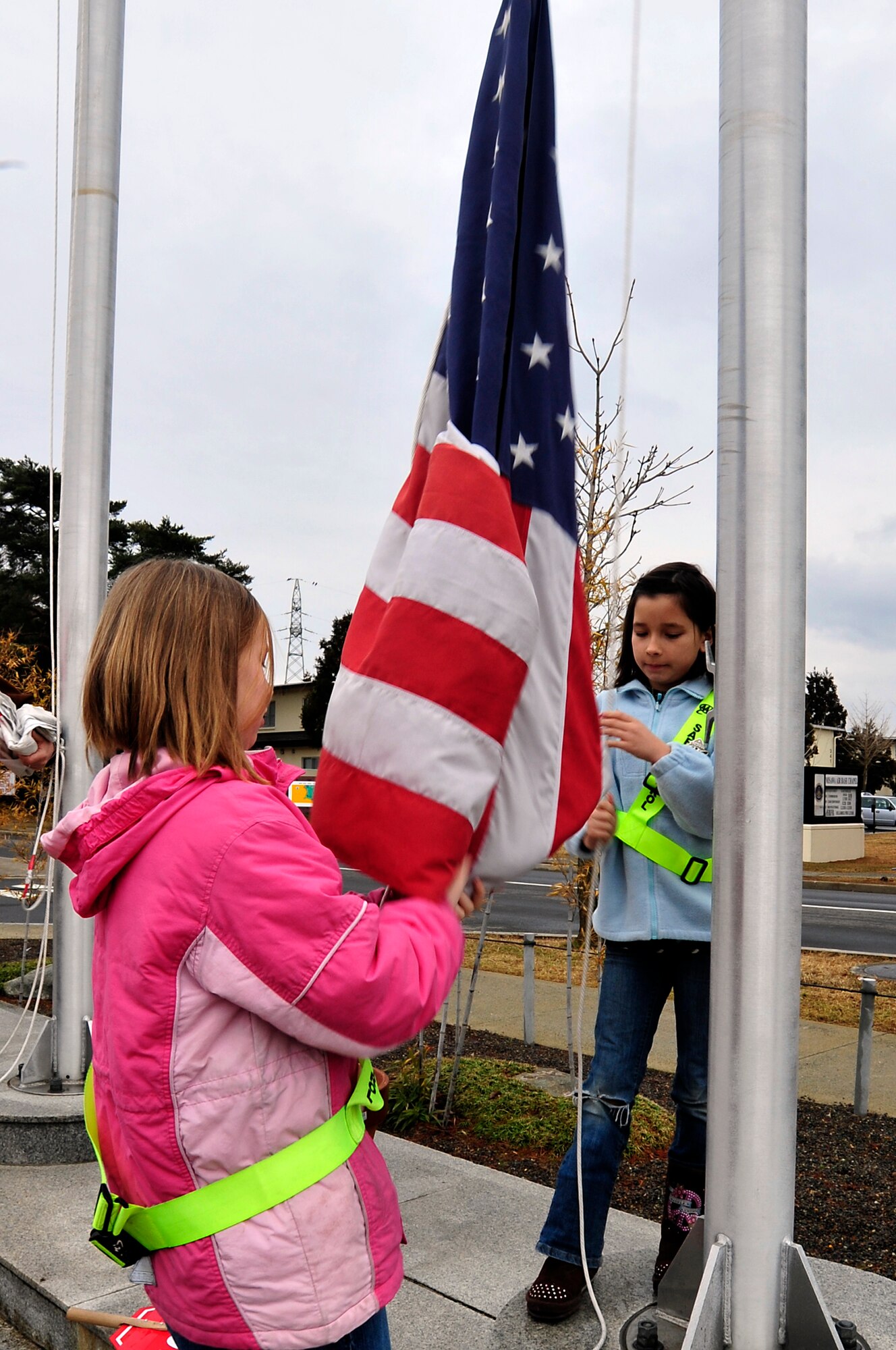 MISAWA AIR BASE, Japan -- Samantha Browning, right, and Hailey Fredrick, both 10-years old, raise the American flag at Sollars Elementary School Mar. 21. Base schools are back in session with all bus routes running and classes starting at the normal times. The schools were closed down for a week after power was knocked out due an earthquake that shook the northern coast of Japan Mar. 11. (U.S. Air Force photo by Staff Sgt. Marie Brown\Released)