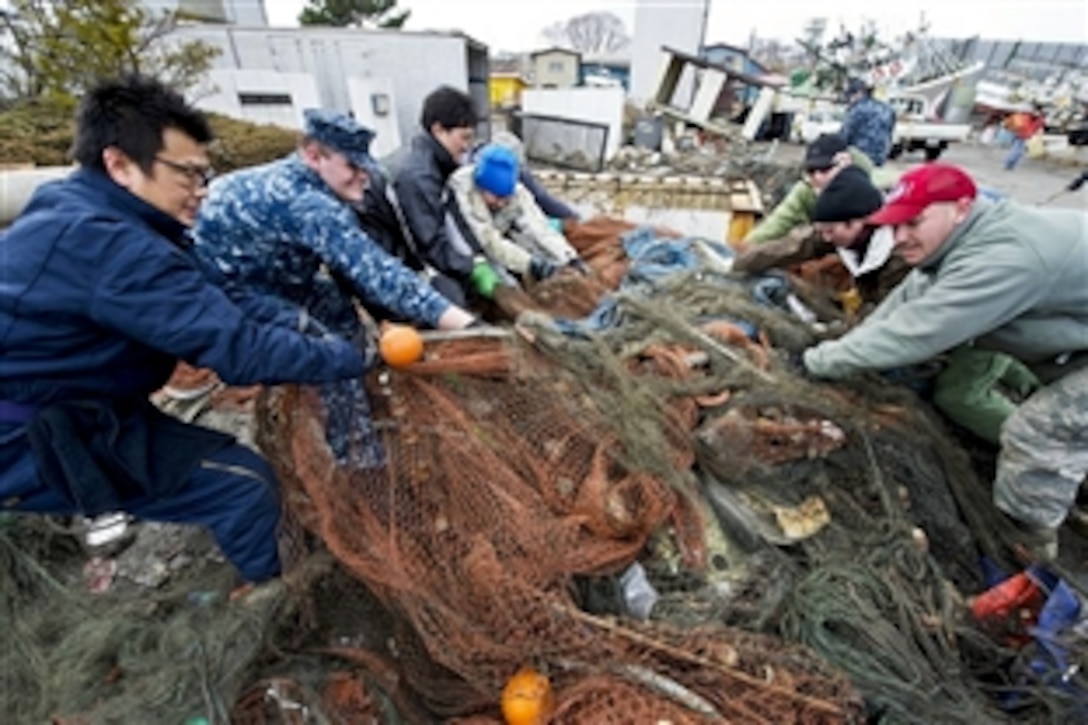 U.S. Navy Petty Officer 2nd Class Gregory Allison, left center, helps local volunteers haul a net filled with debris during relief efforts in the tsunami-battered city of Hachinohe, Japan, March 21, 2011. More than 130 volunteers from Misawa Air Base and members of the French army and Fire Department assisted in a cleanup effort in the northern Japanese city.