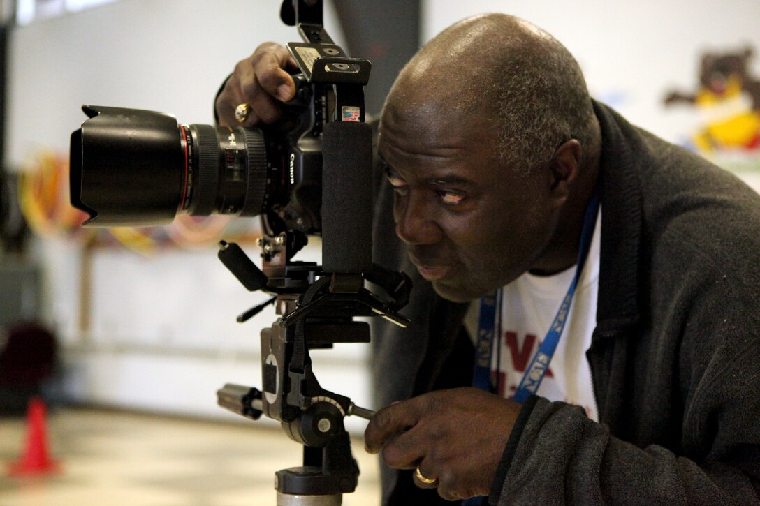 Retired Gunnery Sgt. Johnny M. White, a custodian at the Tarawa Terrace I Primary School and member of the Professional Photographers of North Carolina, peers through his camera's viewfinder at the primary school's gymnasium, March 22.