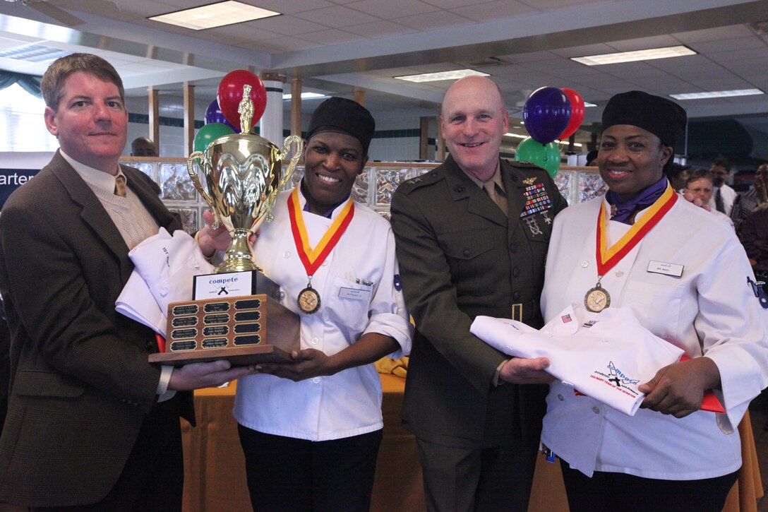 Steve Sherman (left), district manager with Sodexo, and Maj. Gen. Carl B. Jensen, commanding general of Marine Corps Installations – East, present Annette Mageo (left), and Gloria Petteway, cooks with French Creek Mess Hall 420, with their first place awards after this year’s first Culinary Team of the Quarter Competition at Mess Hall 211, March 22. Mageo and Petteway also won the People’s Choice Award during the Mardi Gras themed culinary competition, which featured many traditional Cajun and Creole appetizers, entrees and desserts.::r::::n::