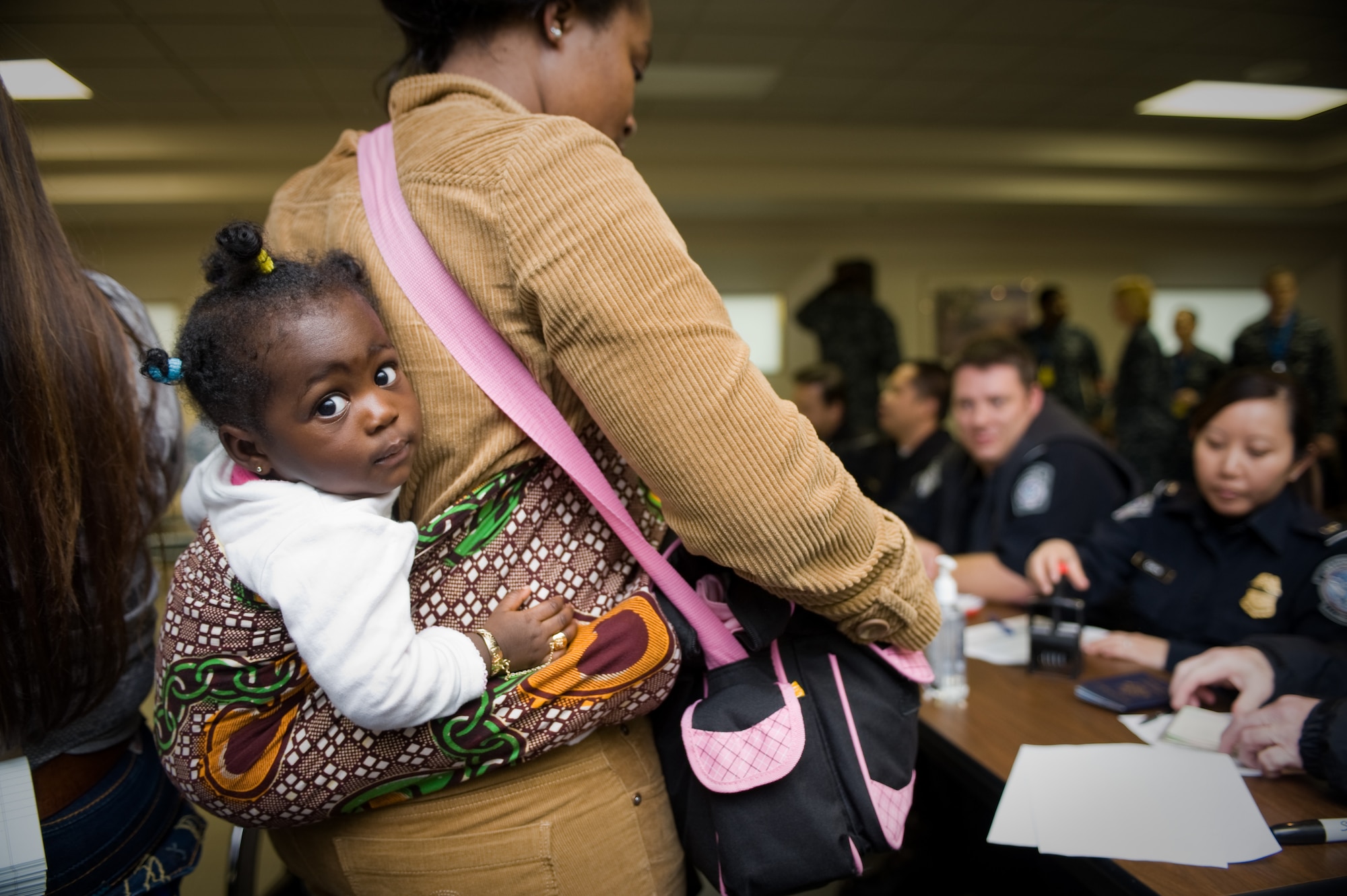 Thirteen-month-old Laila Kpodo looks curiously at the camera while her mother is helped by U.S. Customs and military personnel at Travis AFB, Calif. The mother and daughter were part of approximately 240 military family members who returned to the U.S. from Japan following the March 11, 2011 earthquake and tsunami that hit the island nation. (Photo by Ken Wright)