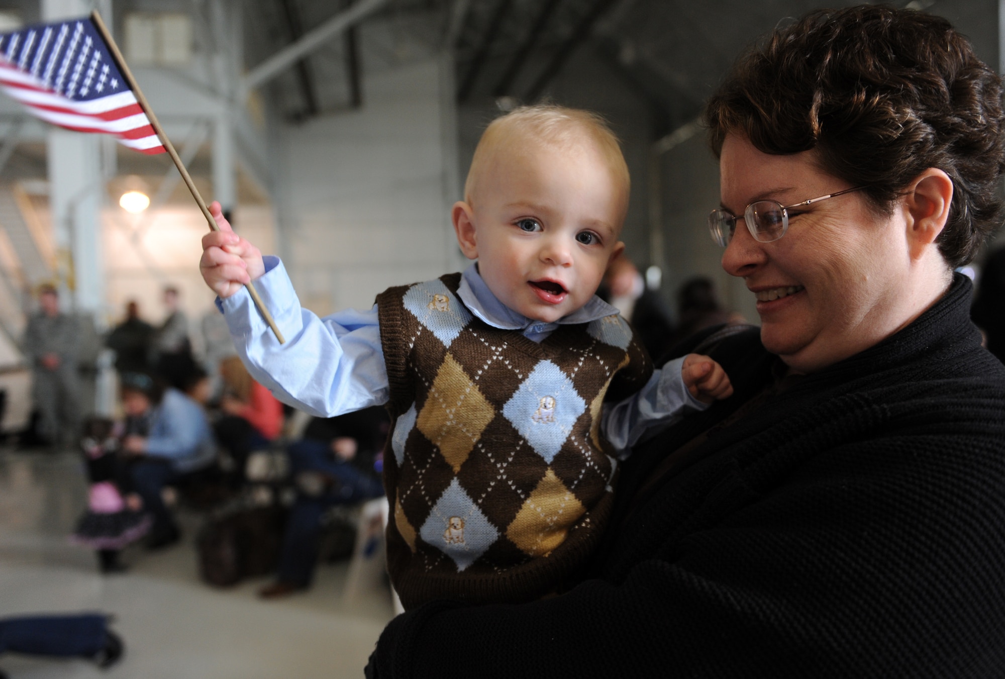 MOUNTAIN HOME AIR FORCE BASE, Idaho – Hayden Kearn, 15 months, waves an American flag with help from his grandmother, Kelley Kearn in hangar 1331 while he waits for his father’s return from a deployment to Southwest Asia, March 19. Approximately 200 Airmen from the 726th Air Control Squadron returned from a deployment in support of Operation New Dawn. The squadron is always prepared to deploy with a mission to provide unparalleled air battle management to joint air, land and sea power anytime, anywhere. (U.S. Air Force photo by Senior Airman Debbie Lockhart)