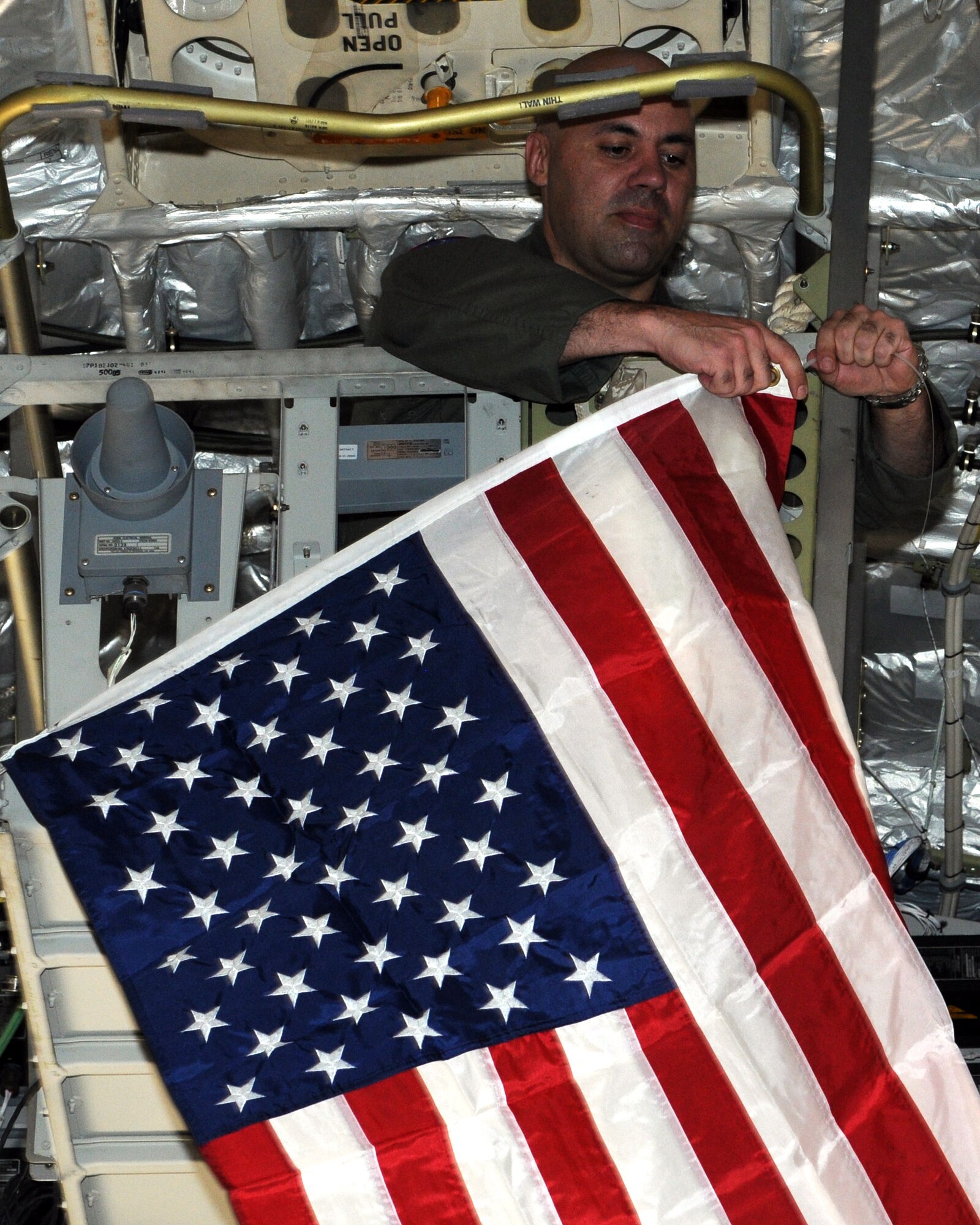 ALTUS AIR FORCE BASE, Okla. -- Capt. Jeremy J. Farlaino, 97th Training Squadron chief of C-17 wing training, hangs an American flag from the cat-walk on a C-17 Globemaster III March 22, before departing to support Operation Odyssey Dawn. Capt. Farlaino is the aircraft commander during this mission. (U.S. Air Force photo by Airman 1st Class Kenneth W. Norman/ Released 97th Air Mobility Wing Public Affairs.)