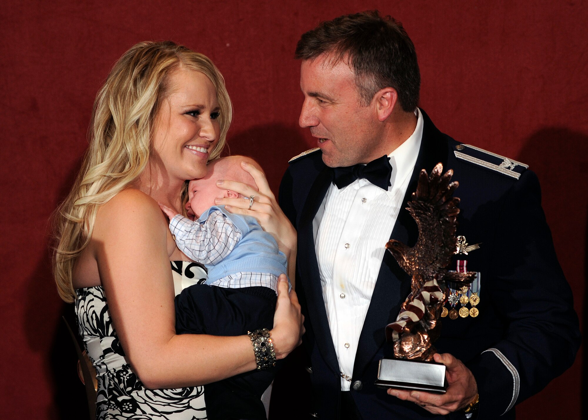 Tiffani Chase, holding her son Landon, accepts the 2010 NCO of the Year award for her husband Tech. Sgt. Daniel Chase. 310th Space Wing Vice Commander Mark Hustedt presented the award to her for the deployed 710th Security Forces member during the wing awards banquet at the Antlers Hilton in Colorado Springs, Colo. (U.S. Air Force photo by Dave Ahlschwede)