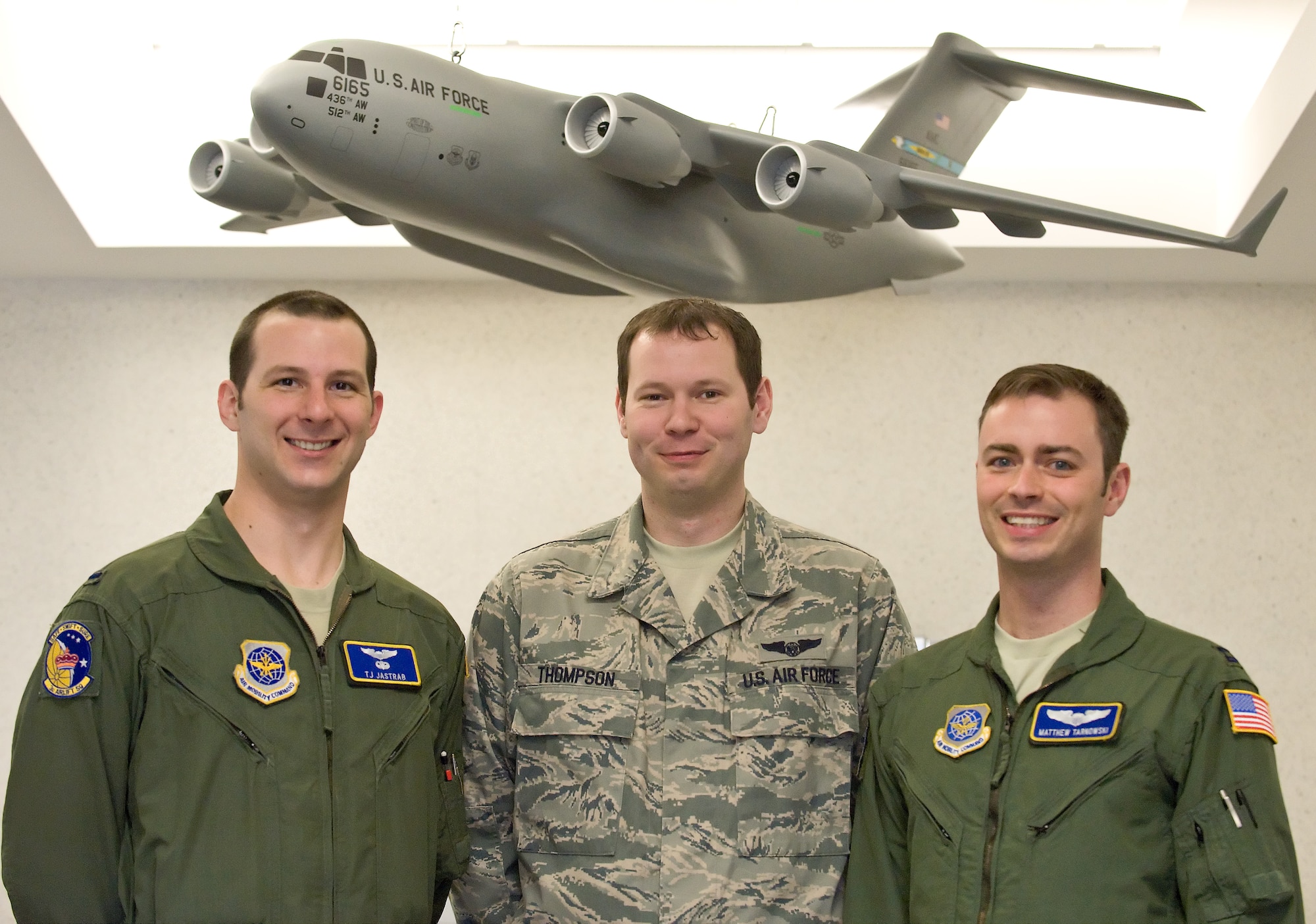 1st Lt. T.J. Jastrab (left), 3rd Airlift Squadron C-17 pilot, Staff Sgt. Ryan Thompson, C-17 loadmaster and Capt. Matt Tarnowski, C-17 aircraft commander, pose underneath a model C-17 March 18, 2011, in the 3rd Airlift Squadron building at Dover Air Force Base, Del. These Airmen were among the members who made the successful delivery of more than 70,000 pounds of humanitarian supplies March 12, 2011, to Misawa Air Base, Japan. (U.S. Air Force photo by Roland Balik)