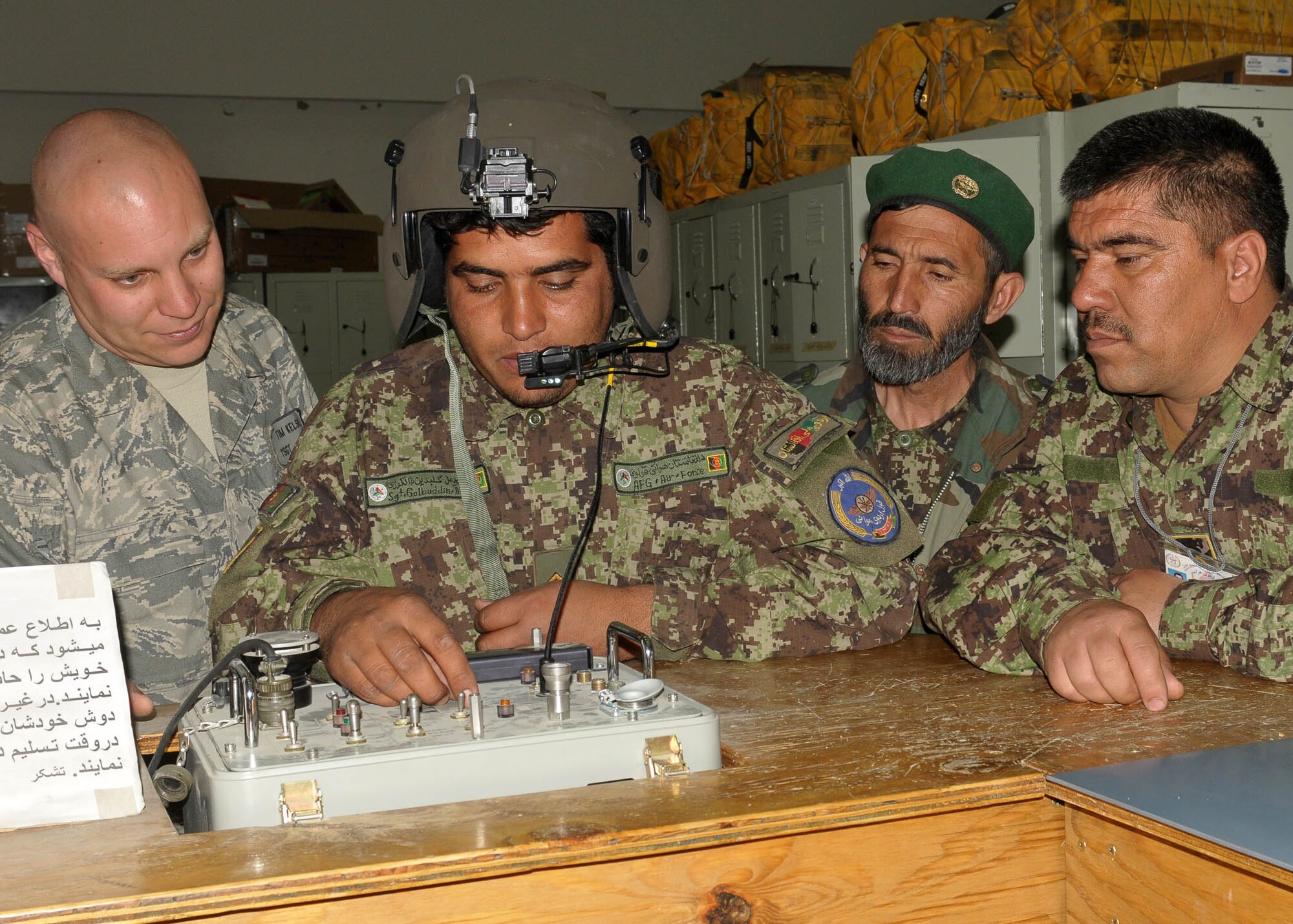 KABUL, Afghanistan - Afghan Air Force member Sgt. Gulbiddin (center), Life Support Specialist, speaks to Tech. Sgt. Tim Kelso (left), Aviation Life Support Advisor for the 838th Air Expeditionary Advisory Group, does a spot check on a helmet to make sure the communication system works.  (U.S. Navy photo by Mass Communications Specialist 3rd Class Jared E. Walker)