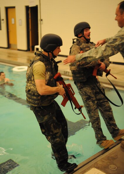 DYESS AIR FORCE BASE, Texas—Senior Airman Kyle Gneuchtel (left) and Tech. Sgt. Mark Thompson (right), 7th Explosive Ordinance Disposal Unit, are pushed into a pool during a two-part training exercise March 22 at the Dyess Fitness Center here. The first part involved removing their flak vest while underwater, swimming 25 meters and rescuing each other from the water. The second part involved push-ups, putting together a pan disrupter and carrying it a quarter-mile, all while wearing an 85-pound bomb suit on the track outside of the fitness center.  EOD conducts training everyday so their Airmen are prepared for challenges they may face. (U.S. Air Force photo/ Airman 1st Class Shannon Hall)