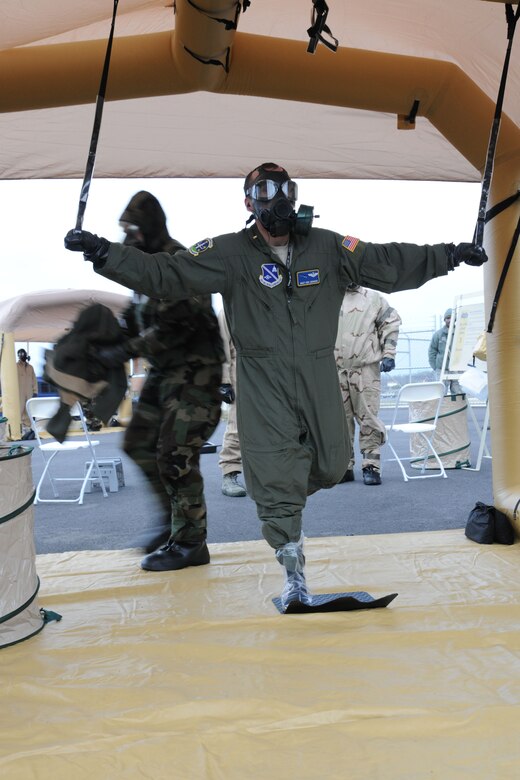 A 1st Helicopter Squadron Airman balances as an aircrew flight equipment Airman removes protective gear during a decontamination exercise March 16.  An example of total force integration between active duty units from Joint Base Andrews and the West Virginia Air National Guard's 167th Airlift Wing, the disbursement exercise allowed all participating units a chance to practice an evacuation of Air Force assets in the event of a chemical attack on the U.S. (U.S. Air Force Photo by Senior Airman Torey Griffith)