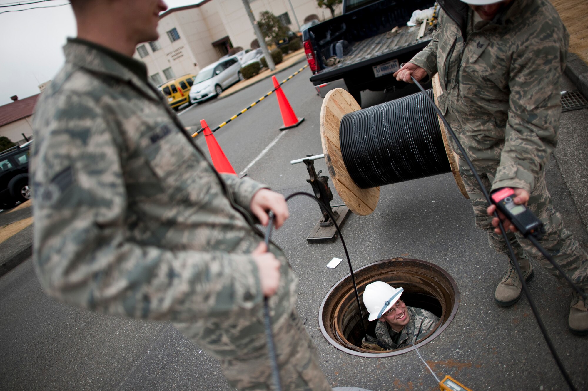 YOKOTA AIR BASE, Japan -- Staff Sgt. Steven Bird, 374th Communications Squadron cable and antenna maintainer, looks up while threading a fiberoptic cable through an underground conduit at Yokota Air Base, Japan, March 23. The cabling provided high-speed network access to a new "tent city" of additional office space for military members stationed here temporarily for Operation Tomodachi. (U.S. Air Force photo/Staff Sgt. Samuel Morse)