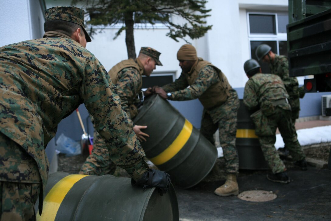Cpl. Tori K. Tadehara, left, a heavy equipment mechanic, Task Force Fuji, III Marine Expeditionary Force Forward, rolls a barrel of kerosene towards one of the drop points.  Marines with Task Force Fuji, III MEF (Fwd), and Japanese Self-Defense Force soldiers unloaded four barrels of kerosene from a convoy here March 24.  The convoy was supplying areas of Japan hardest hit by the earthquake and tsunami.  Shelters, group homes and temporary Japanese Self-Defense Force bases established to conduct disaster relief and humanitarian assistance operations will receive the kerosene to be used as heating fuel.  Throughout the three-day mission, the Marines and sailors of TFF delivered 140 barrels of kerosene while traveling more than 400 miles on mountain roads in temperatures that were frequently below freezing.