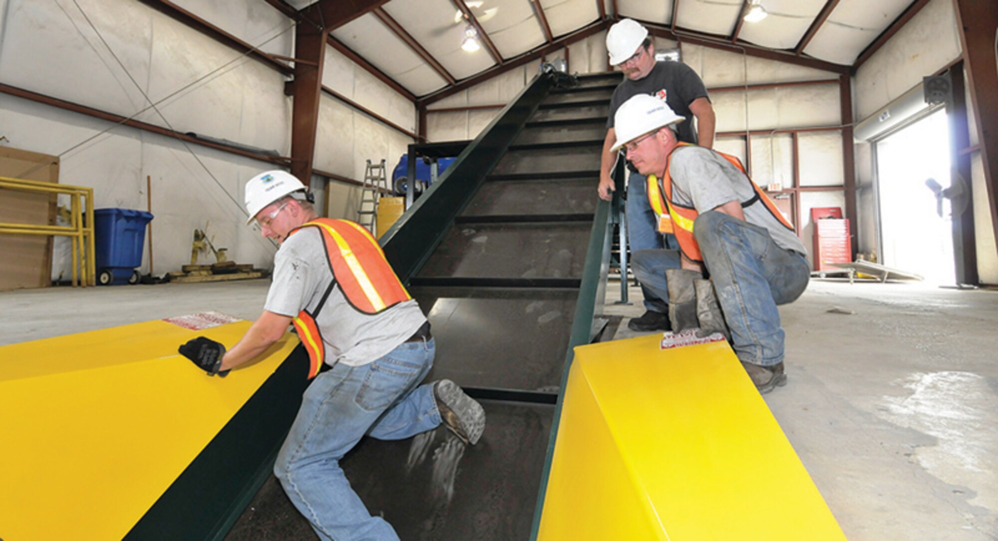 Vick Hobarter, top right, with International Baler, watches as Jay Thurmond, right, and Wyatt James, left, with Recycling Equipment Inc., (REI, Inc.), help to install the conveyer for a newly acquired SST series baler made by International Baler at AEDC’s recycling center. (Photo by: Rick Goodfriend)