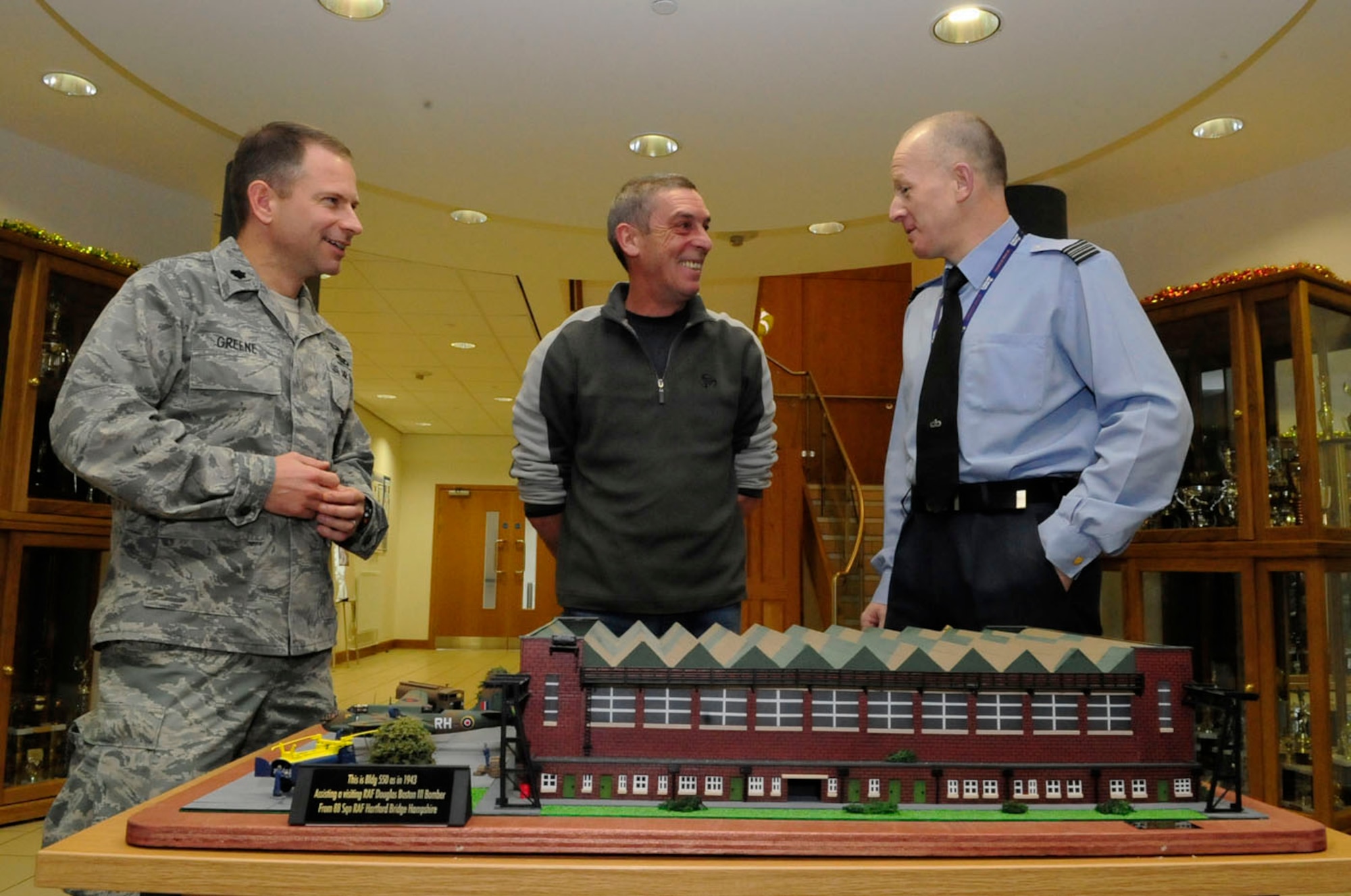 RAF MILDENHALL, England -- Ray Rowson, center, 100th Civil Engineer Squadron and Ministry of Defence employee, chats with Squadron Leader Rick Fryer, RAF Mildenhall Station Commander, and Lt. Col. Matt Greene, 100th CES commander, about the model of Building 550 he recently completed. Mr. Rowson spent a year doing all the advance preparations, taking photos and getting precise measurements, before building the model. It is a replica of one of three original historical hangars here, as it appeared in 1943. The model is now on display upstairs in the Galaxy Club. (U.S. Air Force photo/Senior Airman Ethan Morgan)