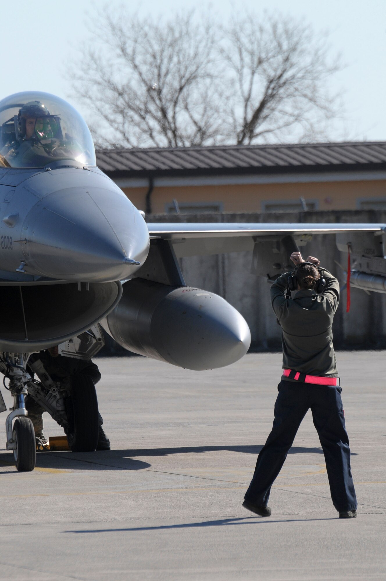 A U.S. Air Force flight crew member guides an F-16 Fighting Falcon pilot at Aviano Air Force Base, Italy, after supporting Operation Odyssey Dawn on March 20, 2011. Joint Task Force Odyssey Dawn is the U.S. Africa Command task force established to support the larger international response to the unrest in Libya.  A broad coalition of nations are partnering to enforce U.N. Security Council Resolution (UNSCR) 1973, which authorizes all necessary means to protect civilians in Libya under threat of attack by Qadhafi regime forces.  JTF Odyssey Dawn is commanded by Admiral Samuel J. Locklear, III. (US Army Photo by SSG Tierney P. Wilson) 
