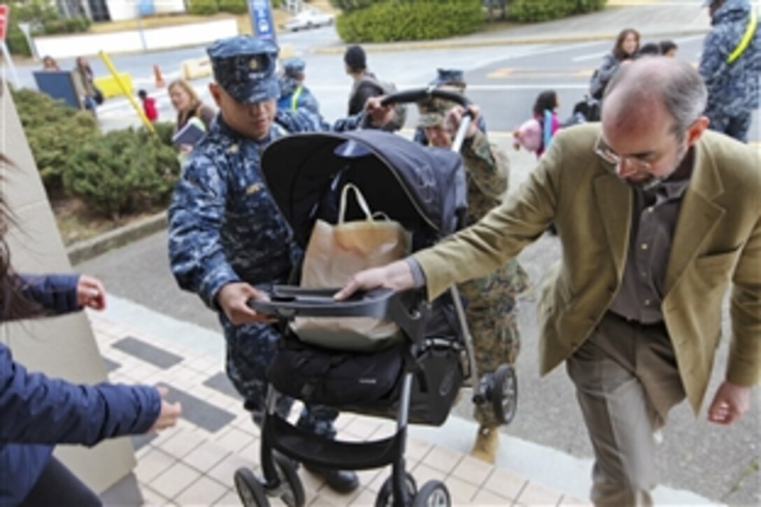 U.S. Marine Corps Lt. Gen. Terry G. Glueck, center, and Raymond Greene, right, assist a Navy family with their stroller at a voluntary departure check point during a visit to the 3rd Marine Expeditionary Brigade Aviation Command Element  in Atsugi, Japan, March 24, 2011. The U.S. is providing support to Japan following the recent earthquake and tsunami. Glueck is commander of the III Marine Expeditionary Force and Greene is the U.S. consul general in Okinawa.
