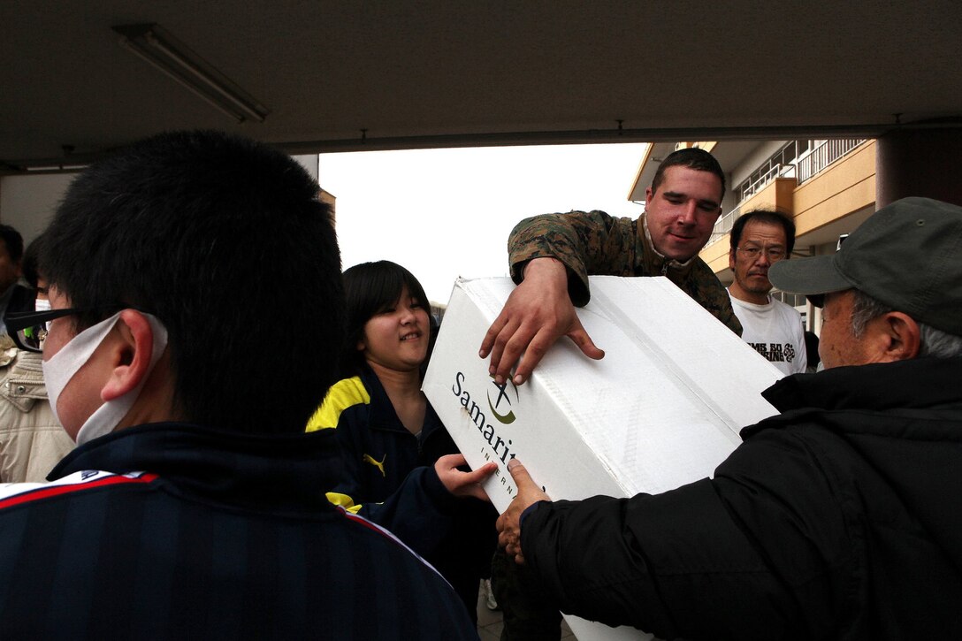 Lance Cpl. Matthew Goeringer passes a box of hygiene items with Japanese civilians, March 25. Service members with United States Forces Japan (Forward) and Japanese North East Army delivered 500 hygiene sets, toys, and clothes to the Okuma Elementary School for internally displaced personnel. The donations were provided by Samaritan’s Purse. Goeringer is a bulk fuel specialist with Task Force Fuji.