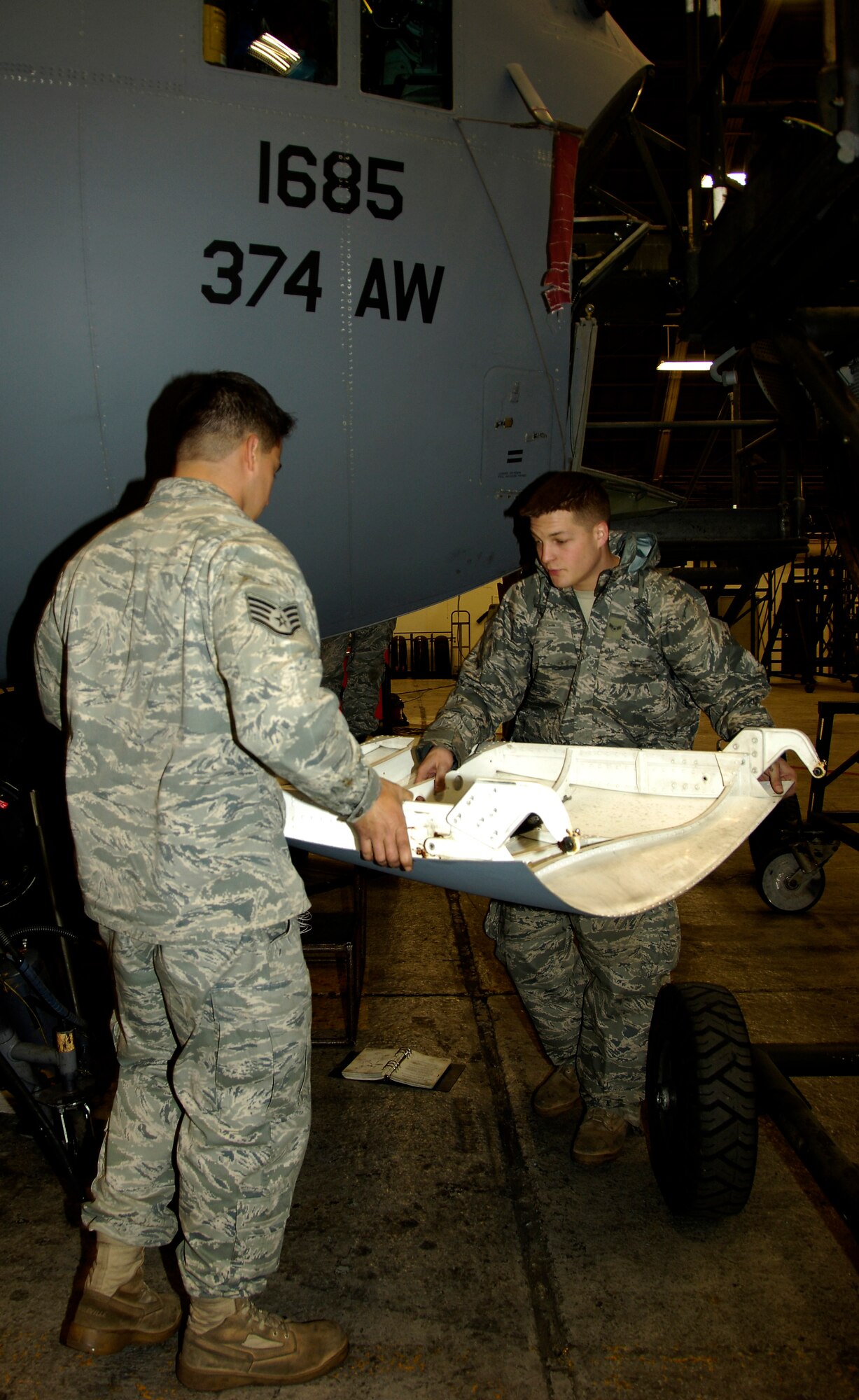 YOKOTA AIR BASE, Japan -- Airman 1st Class Travis Farr (right) and Staff Sgt. Alex Montero carry a C-130 Hercules forward landing gear door to a storage rack March 25, 2011. Removing the door helps electricians complete necessary repairs easier. The C-130 is undergoing routine maintenace in preparation to support Operation Tomodachi. Both Airmen are crew chiefs with the 374th Maintenance Squadron. (U.S. Air Force photo/ Staff Sgt. J.G. Buzanowski)