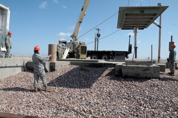 Airman 1st Class Nicholas Wells and Airman 1st Class Mark Carrier, both from 90th MMXS, hold the tag lines of the diesel cover as it is raised while 2nd Lt. Clinton Chandler, 90th MMXS, observes the process. Staff Sgt. James Strickland, 90th MMXS, spots the cover from below as it is being lowered into the exhaust shaft during the replacement of the launch facilities back-up power supply with a new diesel engine March 18. (U.S. Air Force photo by Blaze Lipowski)