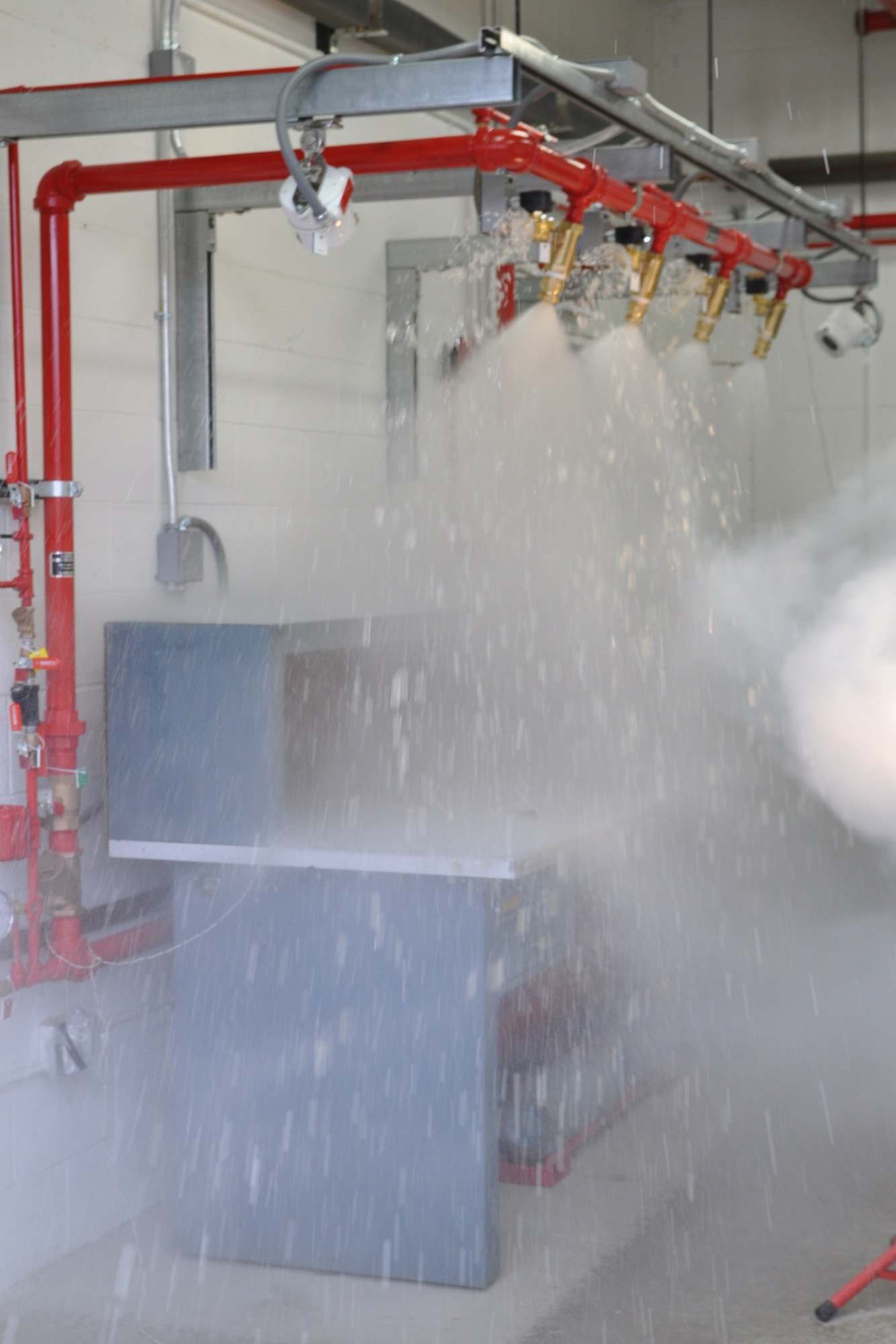 YOUNGSTOWN AIR RESERVE STATION, Ohio -- This is the third of three photos showing the successful test of a Hgh-Speed Deluge System mounted above a work table in a muntions processing building here, March 24. The elapsed time between the first and thrid photos is approximately 100 milliseconds, or one-tenth of a second. In this third photo, water continues to pour from the deluge system to completely extinguish the test heat source. The system, the first of its kind installed on an U.S. Air Force installation, is designed to react to an extreme heat source on the table within one hundred milliseconds, or one-tenth of a second, by spraying approximately 300 gallons of water onto the table to extinguish any accidental ignition of munitions to protect personnel and property. U.S. Air Force photo by Master Sgt. Bob Barko Jr.