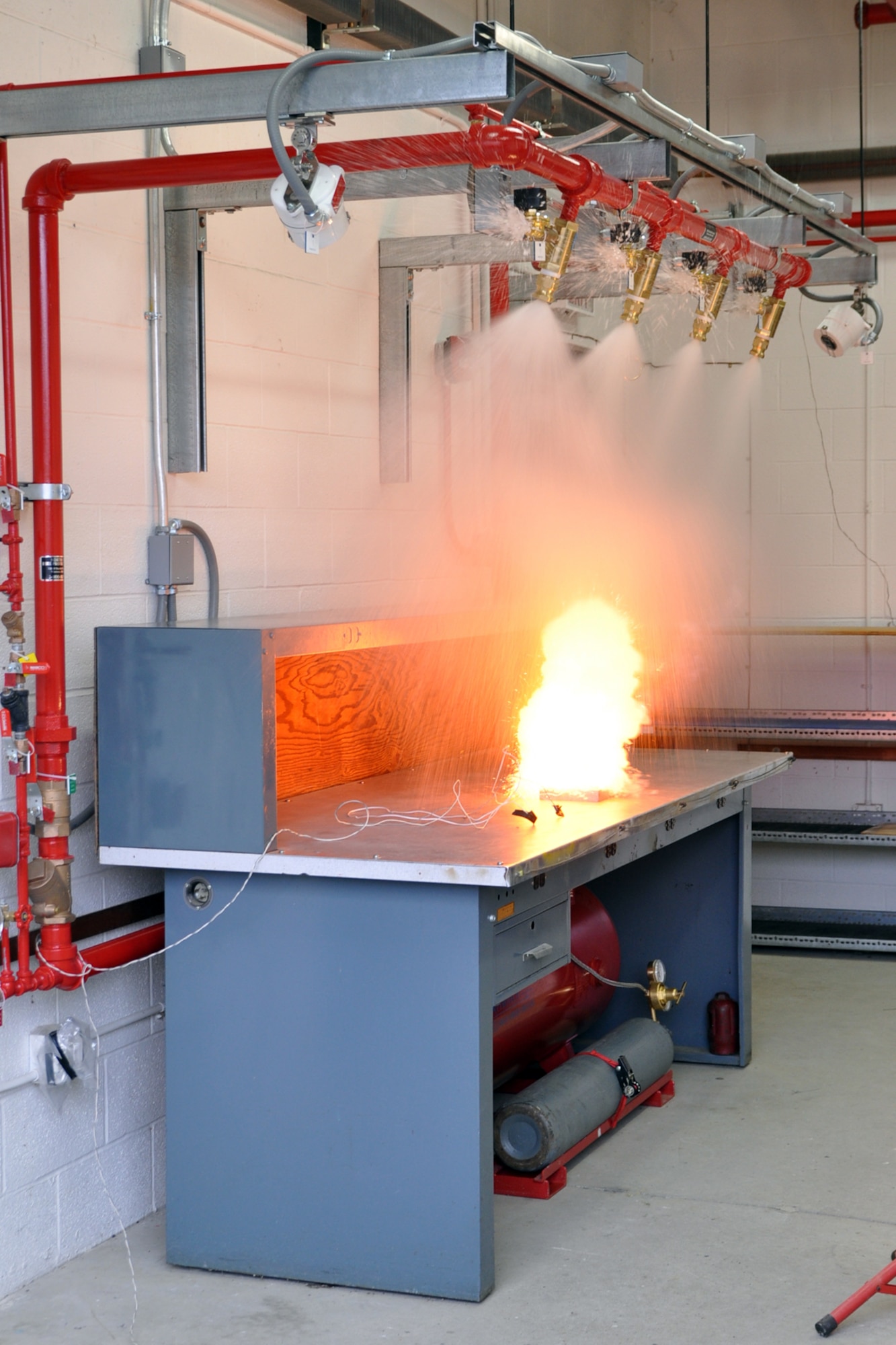 YOUNGSTOWN AIR RESERVE STATION, Ohio -- This is the second of three photos showing the successful test of a Hgh-Speed Deluge System mounted above a work table in a muntions processing building here, March 24. The elapsed time between the first and thrid photos is approximately 100 milliseconds, or one-tenth of a second. In this second photo, water begins to spray from the deluge system at the moment the heart source for the test, black powder poured over a blasting cap, is ignited by a remote detonator. The system, the first of its kind installed on an U.S. Air Force installation, is designed to react to an extreme heat source on the table within one hundred milliseconds, or one-tenth of a second, by spraying approximately 300 gallons of water onto the table to extinguish any accidental ignition of munitions to protect personnel and property. U.S. Air Force photo by Master Sgt. Bob Barko Jr.
