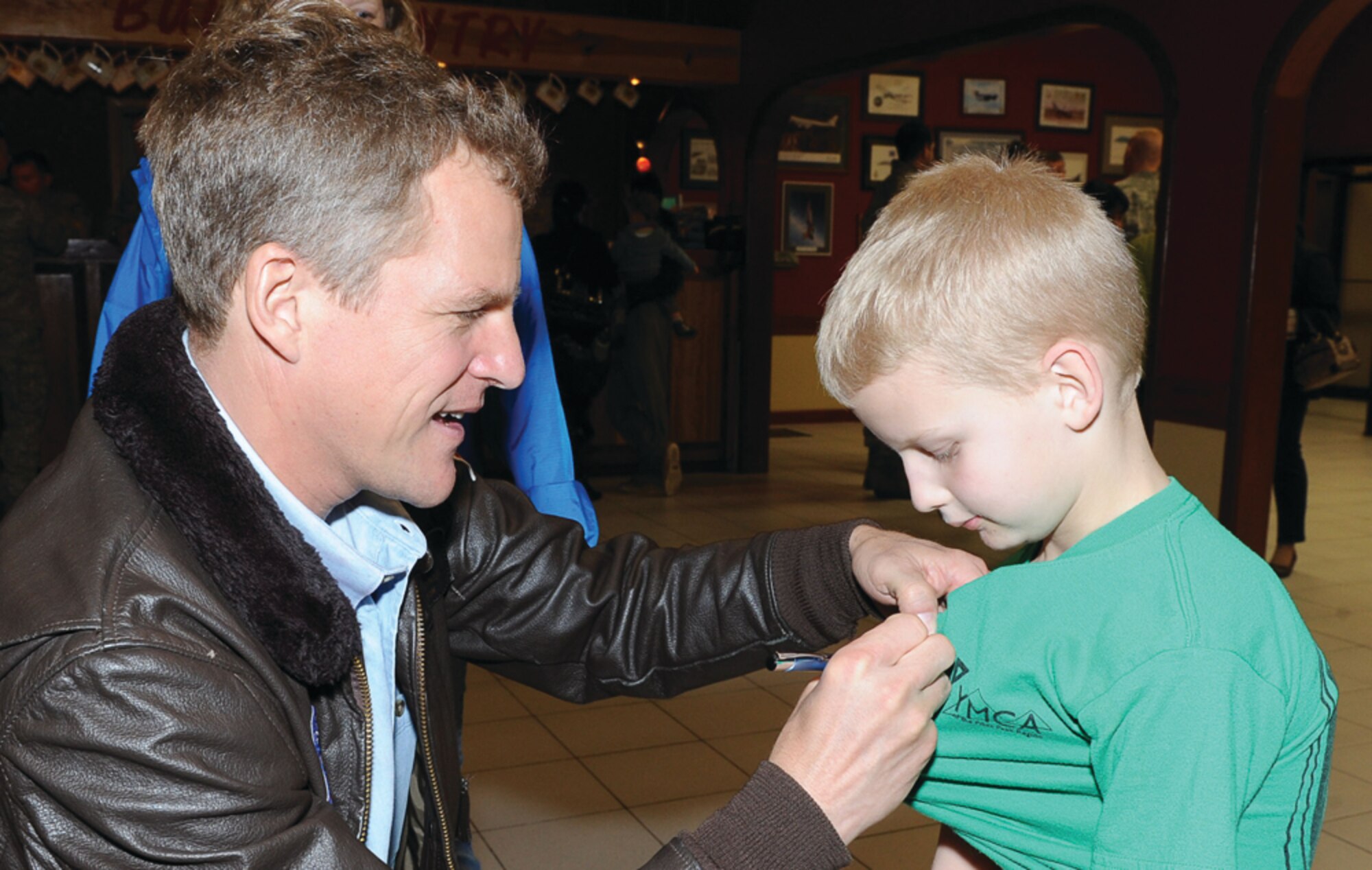 Dr. Scott E. Parazynski signs an autograph on Clayton Gleason's T-shirt during a visit to the 65th Operations Support Squadron March 17, 2011.  Clayton is the son of Maj. Ross Gleason, 65th Civil Engineer Squadron. Dr. Parazynski, accompanied by his son, Luke, also visited and talked with students about his space shuttle voyage to the orbit.  (Photo by Guido Melo)